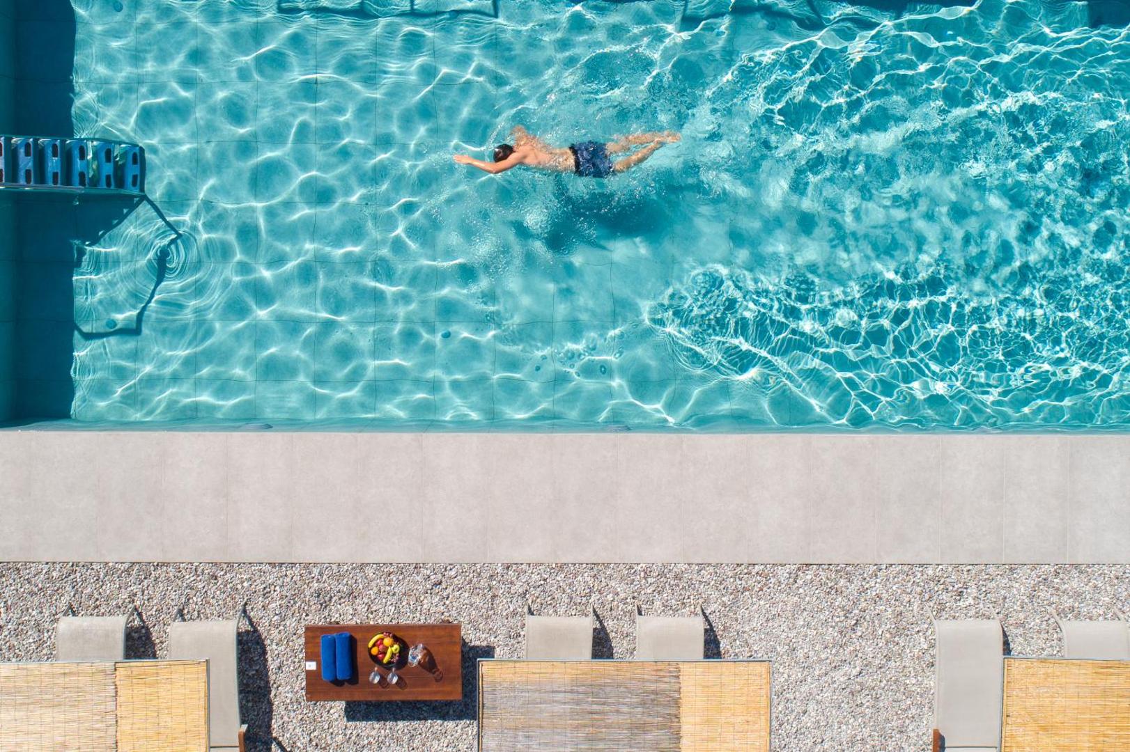 Rodostamo Hotel & Spa skats no augšas uz āra baseinu, kurā peld viesis, blakus atpūtas zona ar augļiem un dzērieniem