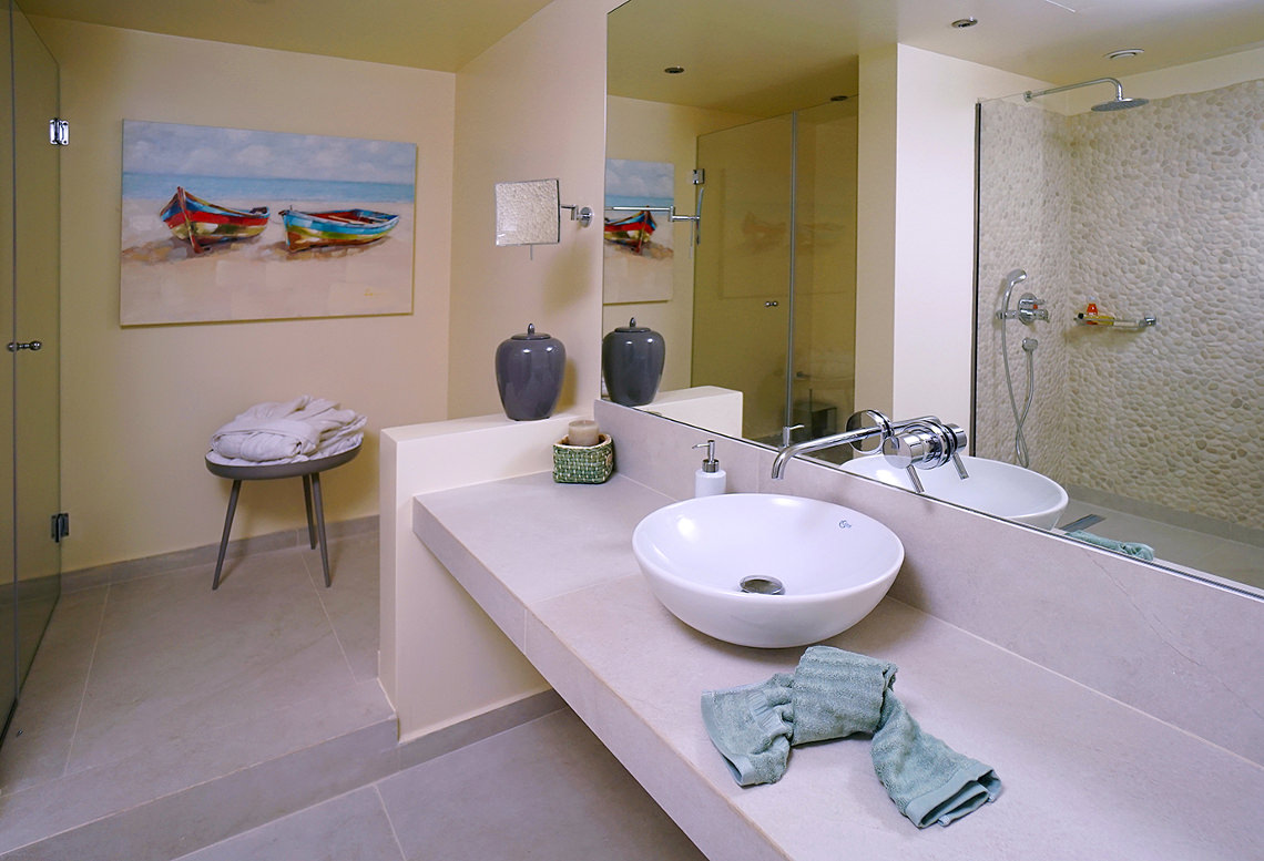 Rodostamo Hotel & Spa numura vannas istaba ar akmens mozaīkas dušu, modernu izlietni un gaišu interjeru — elegants dizains atpūtai Korfu