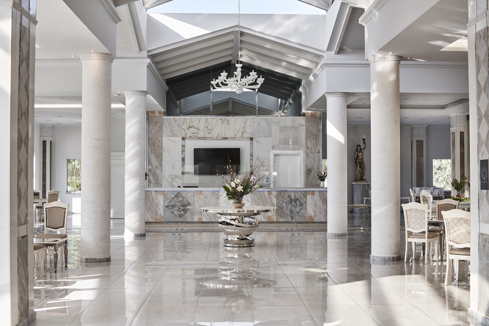 Sandy Villas Resort plašais un gaišais vestibils ar marmora grīdām, kolonnām un modernu recepcijas zonu, lieli logi un dabīgais apgaismojums.