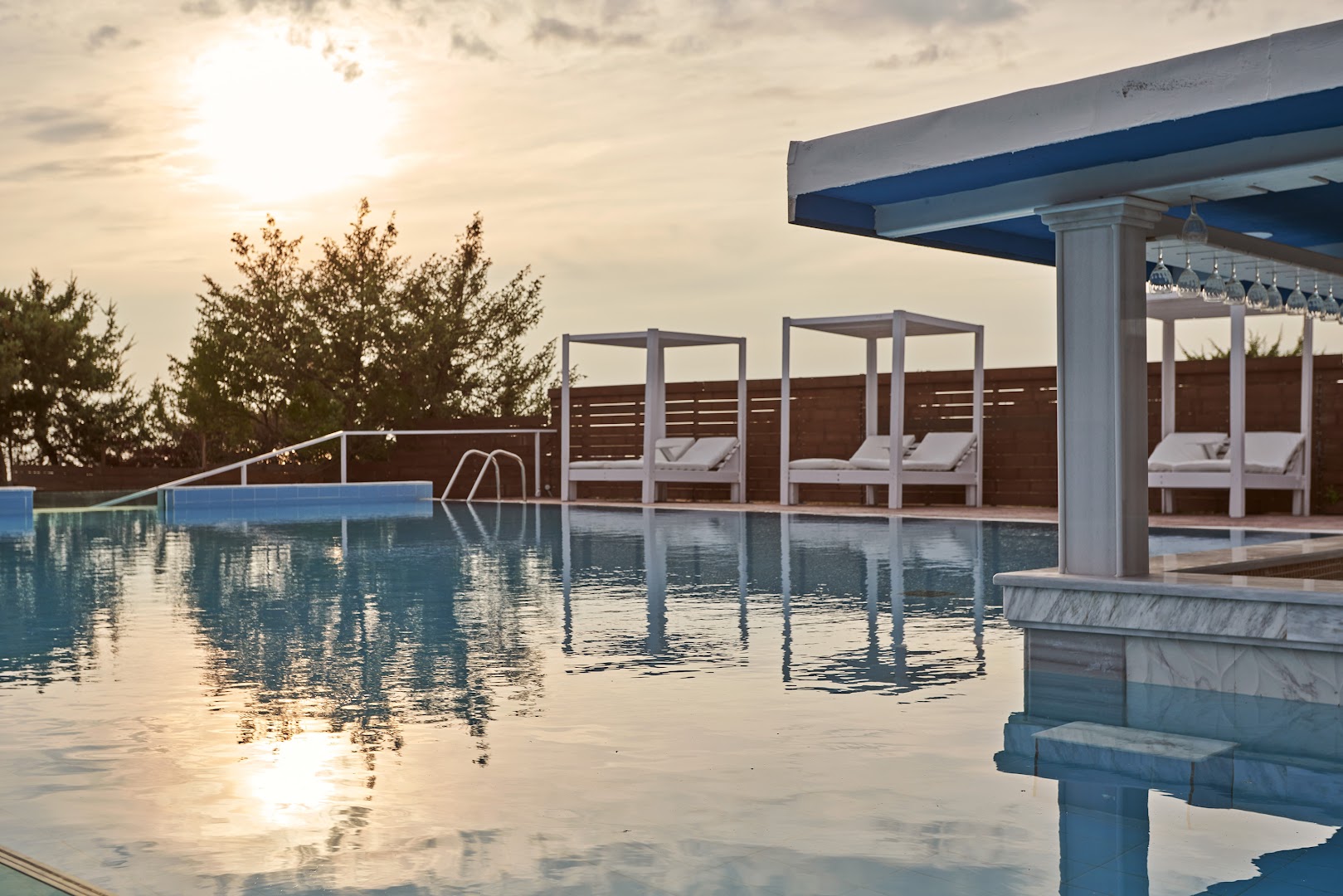 Sandy Villas Resort baseina bārs un atpūtas gultas ar baldahīniem saulrieta laikā — romantiska atmosfēra vakarā pie ūdens