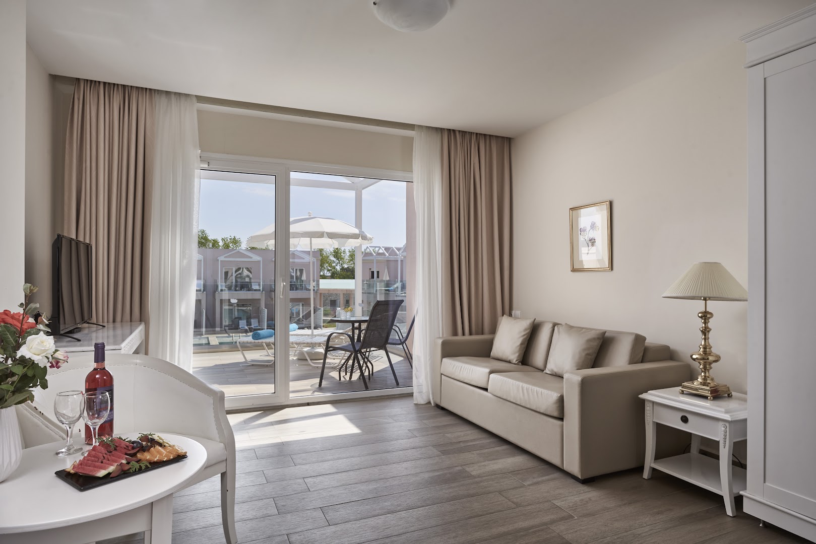 Sandy Villas Resort viesistabas zona ar dīvānu un skatu uz privāto terasi, kur redzami sauļošanās krēsli un saulessargs