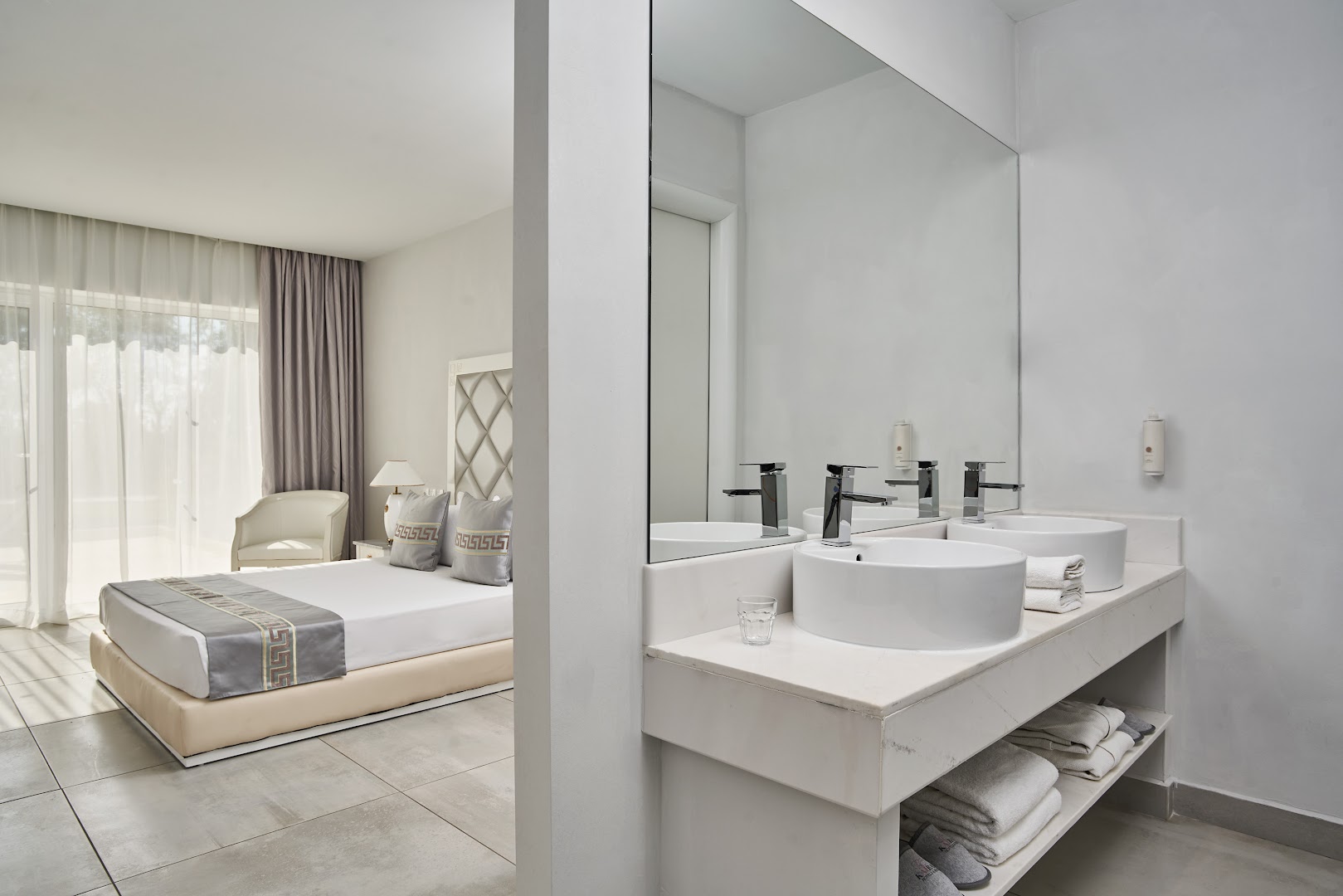 Sandy Villas Resort moderns numurs ar gaišu interjeru, divguļamo gultu un atvērtā plānojuma vannas istabu ar divām izlietnēm un lielu spoguli.