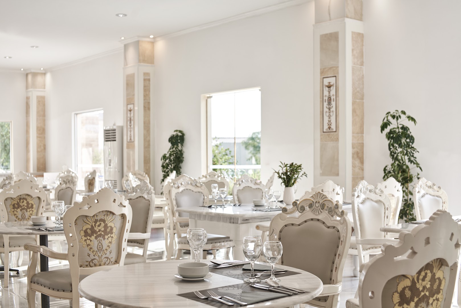 Sandy Villas Resort elegantais iekštelpu restorāns ar grezniem krēsliem un marmora galdiem, gaišs interjers ar klasiskiem dizaina elementiem.