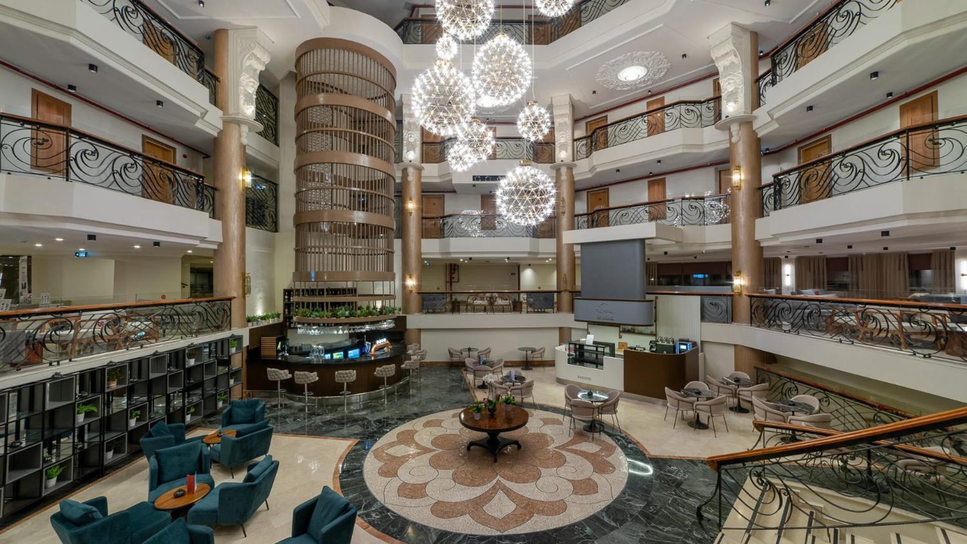 Numa Club Side viesnīcas lobby halle ar modernām lustrām, bāru un atpūtas zonām vairākos stāvos — skats uz interjeru