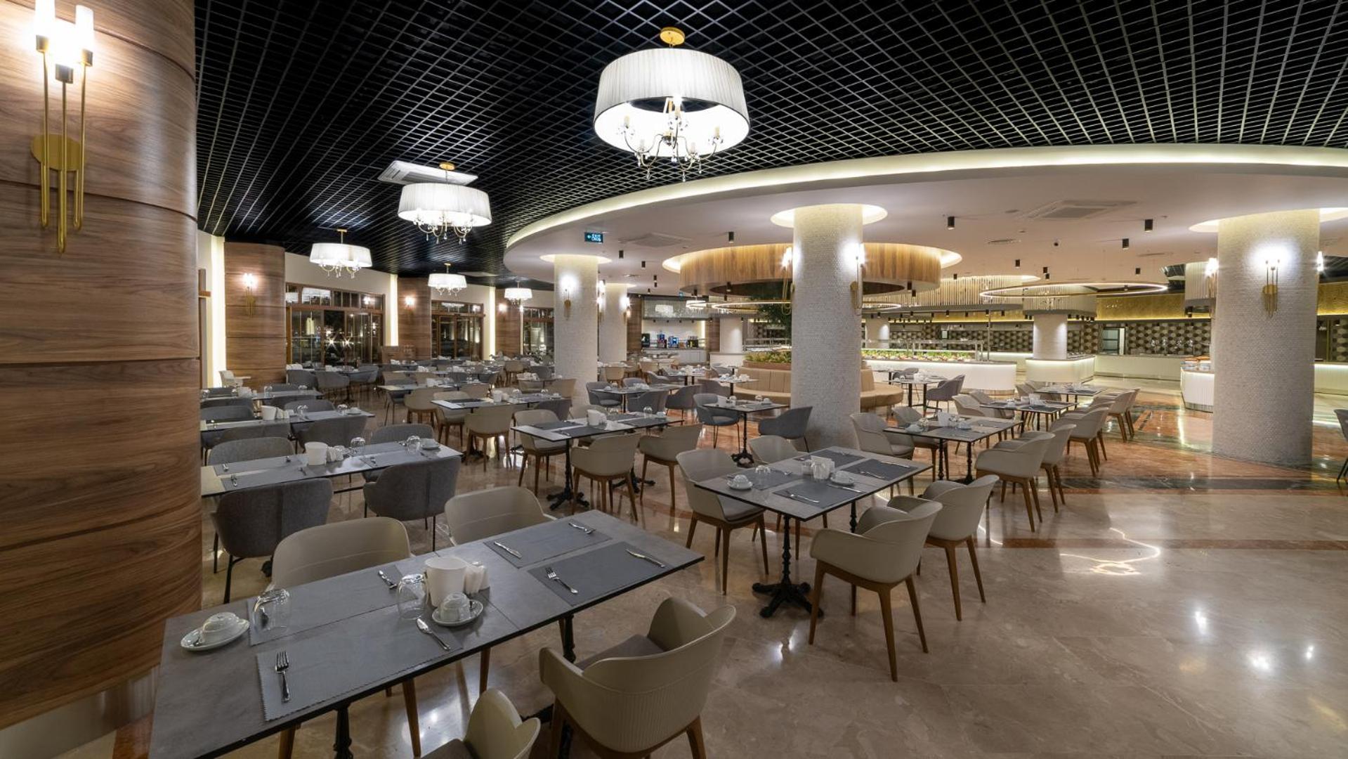 Plašs Numa Club Side viesnīcas restorāns ar daudziem galdiņiem, modernām lustrām un gaišu marmora grīdu Sidē