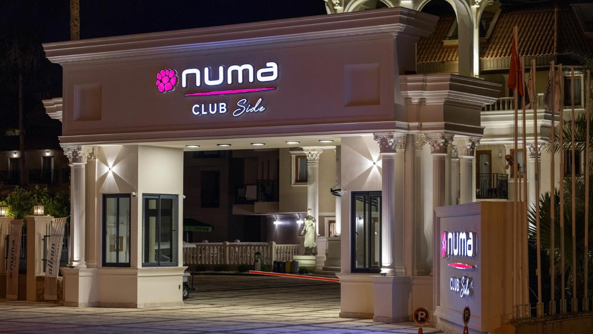 Numa Club Side izgaismotais logo un iebrauktuve nakts laikā, uzsverot viesnīcas moderno un viesmīlīgo tēlu