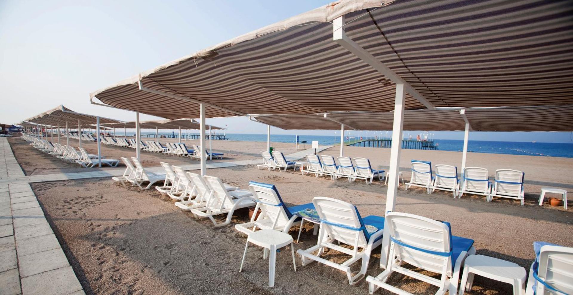 Sunis Elita Beach Resort plašā smilšu pludmale ar saulessargiem un gultām pie zilās jūras Sides piekrastē