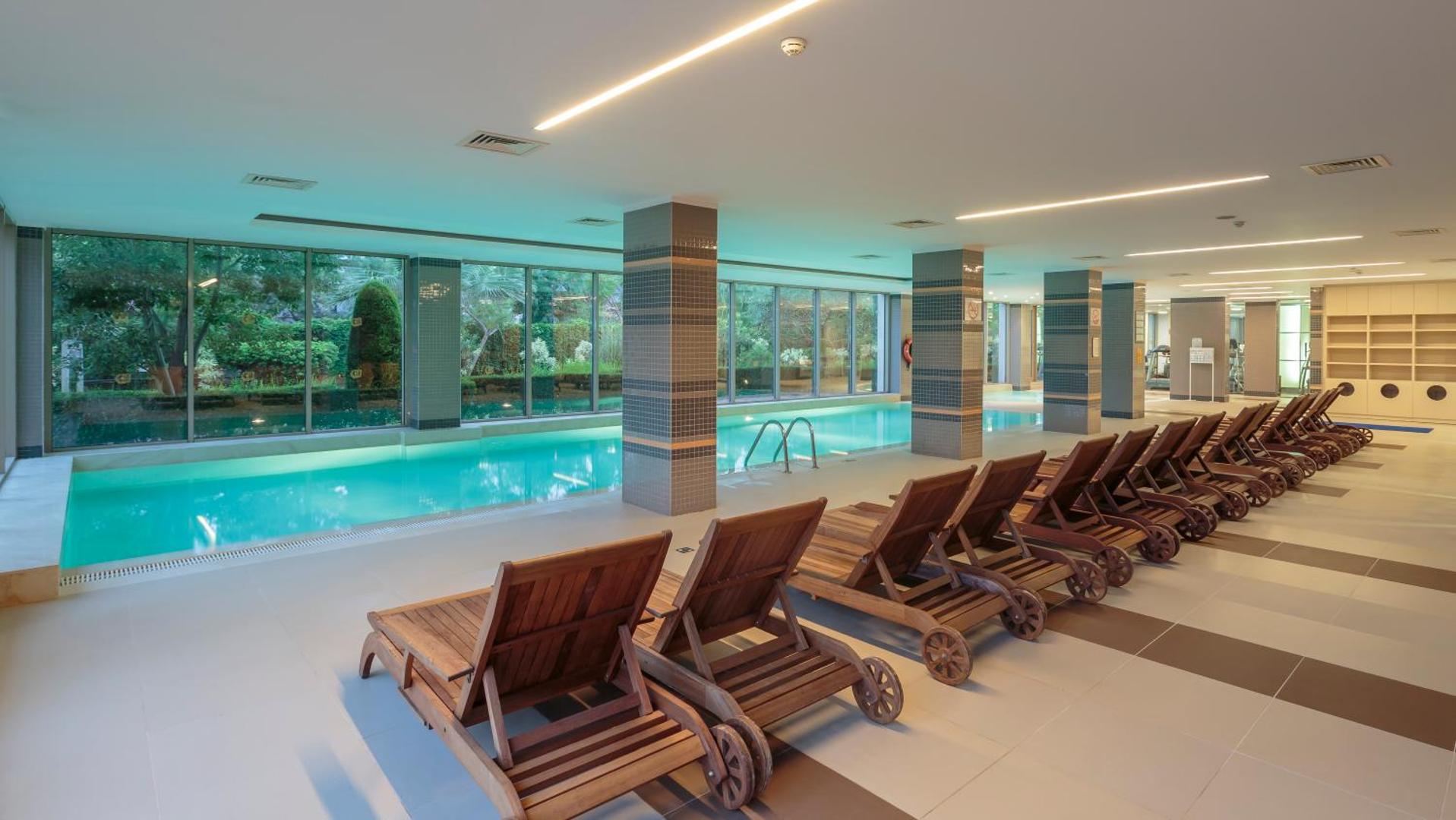 Sunis Elita Beach Resort iekštelpu baseins ar koka sauļošanās krēsliem un lieliem logiem uz dārzu spa centrā