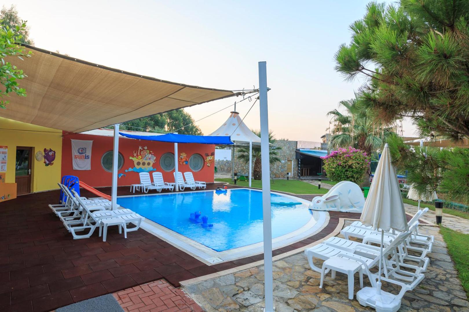 Sunis Elita Beach Resort bērnu baseins ar slidkalniņu un saulessargiem Sides reģionā, Turcijā — atpūtas zona ar baltiem sauļošanās krēsliem