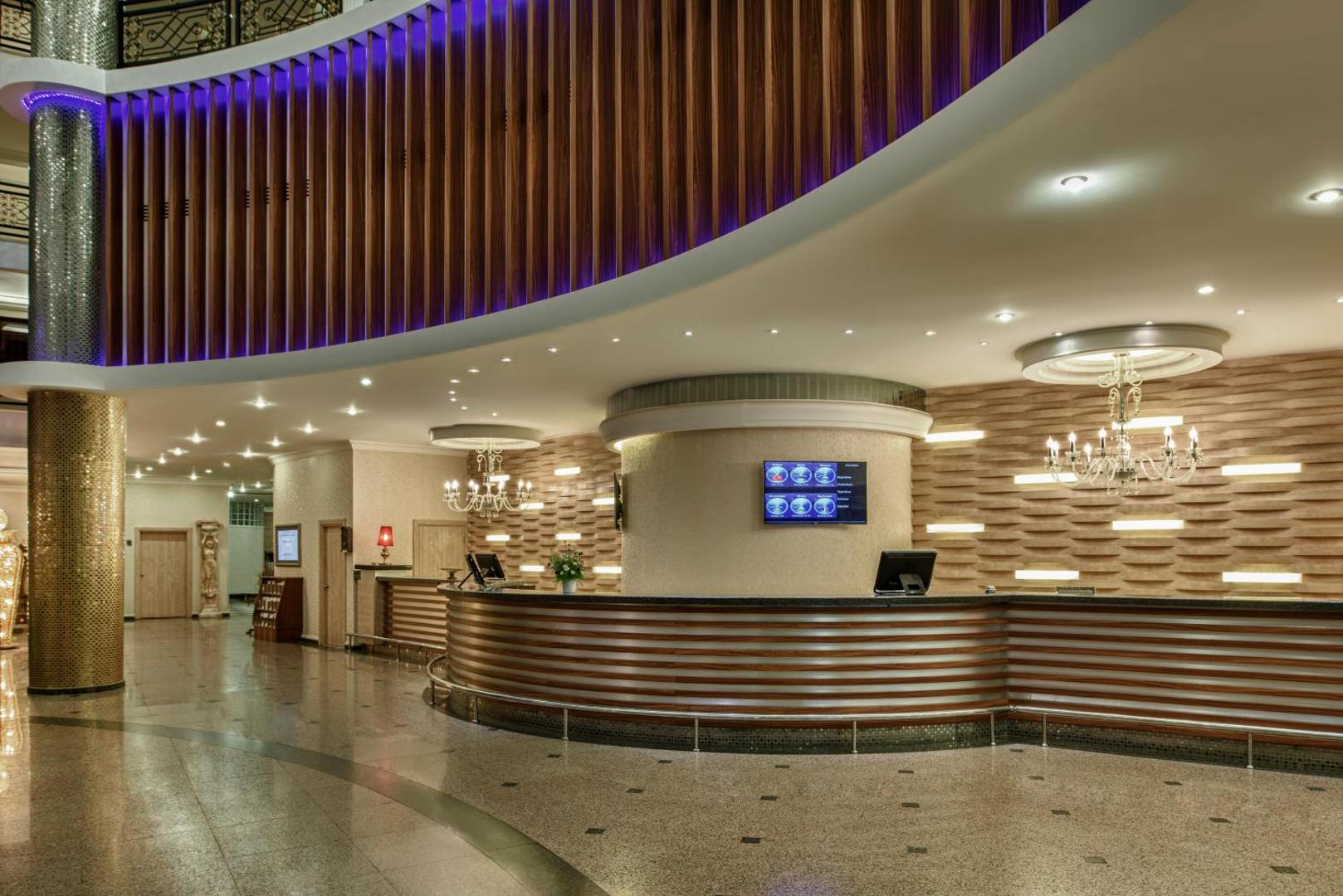 Delphin Deluxe viesnīcas recepcijas zona Alanjā ar modernu koka apdari, elegantām lustrām un plašu reģistrācijas leti viesu uzņemšanai