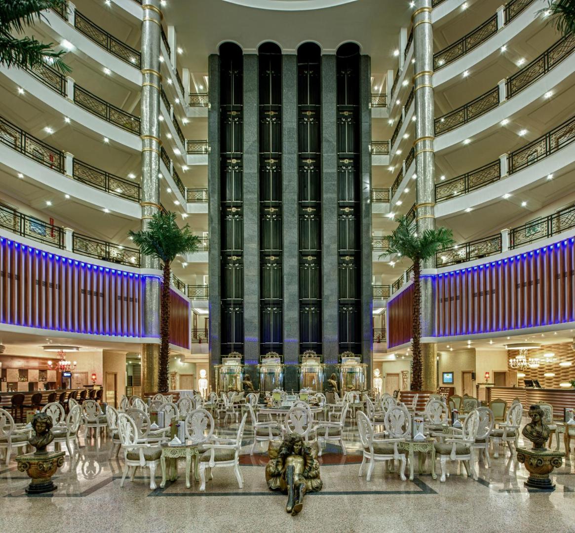 Delphin Deluxe viesnīcas iespaidīgais vestibils ar vairākiem stāviem, panorāmas liftiem, palmām un klasiska stila mēbelēm