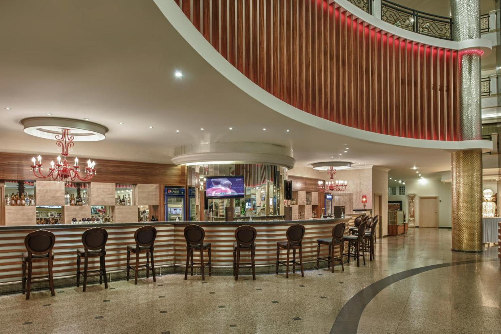 Delphin Deluxe viesnīcas lobby bārs ar pusapaļu leti, augstiem krēsliem un mājīgu apgaismojumu vakara kokteiļu baudīšanai