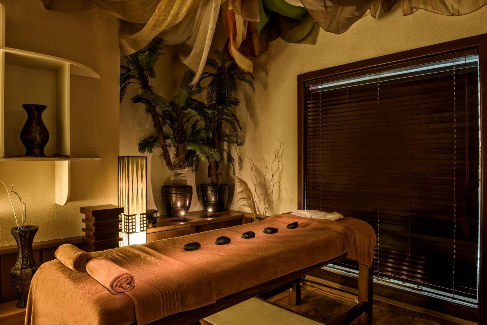 Delphin Deluxe spa centra masāžas telpa ar siltu apgaismojumu, akmeņu terapijas piederumiem un eksotisku interjeru relaksācijai