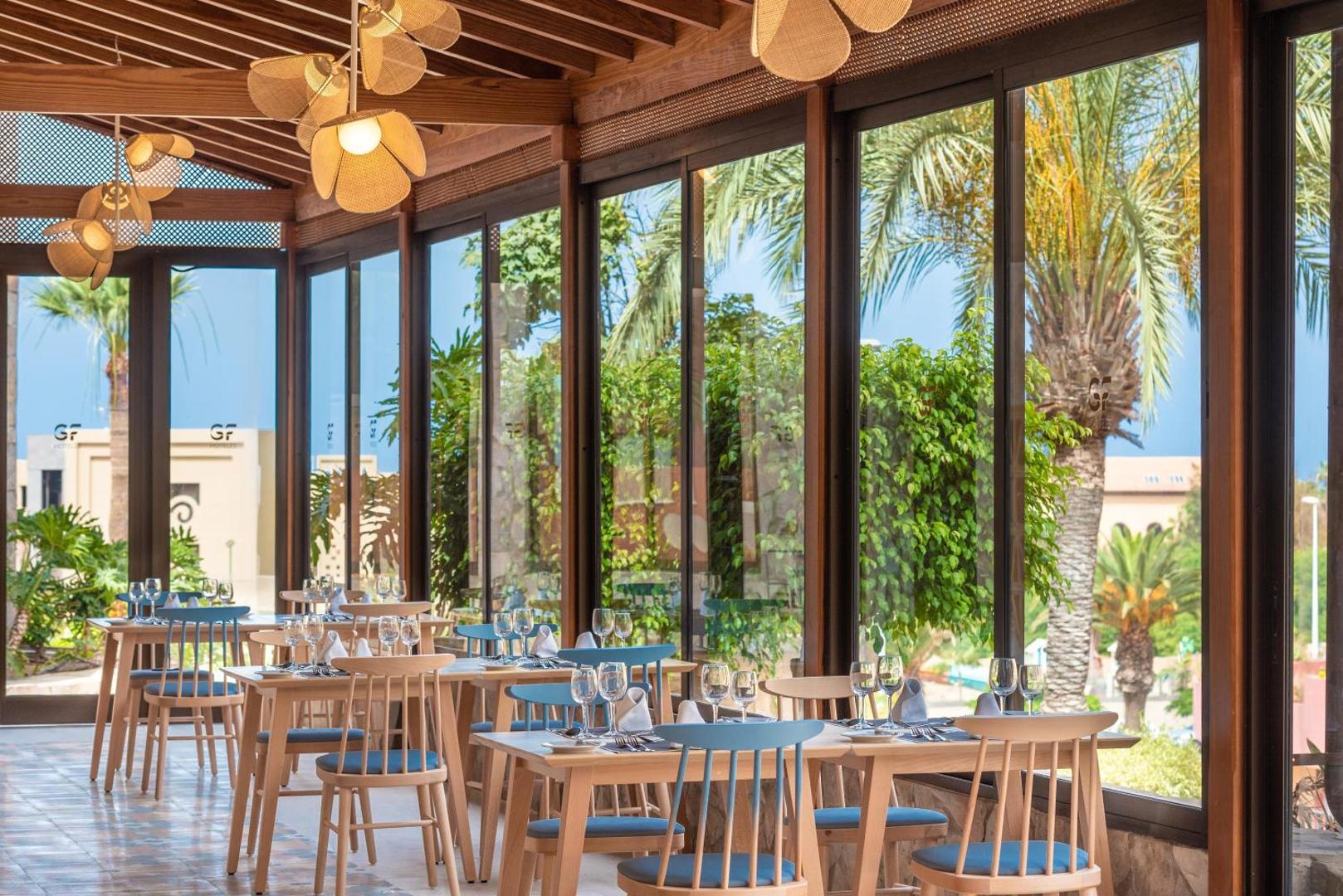 GF Gran Costa Adeje viesnīcas restorāns ar panorāmas logiem Tenerifē — gaišs interjers, koka griesti un skats uz palmu dārzu