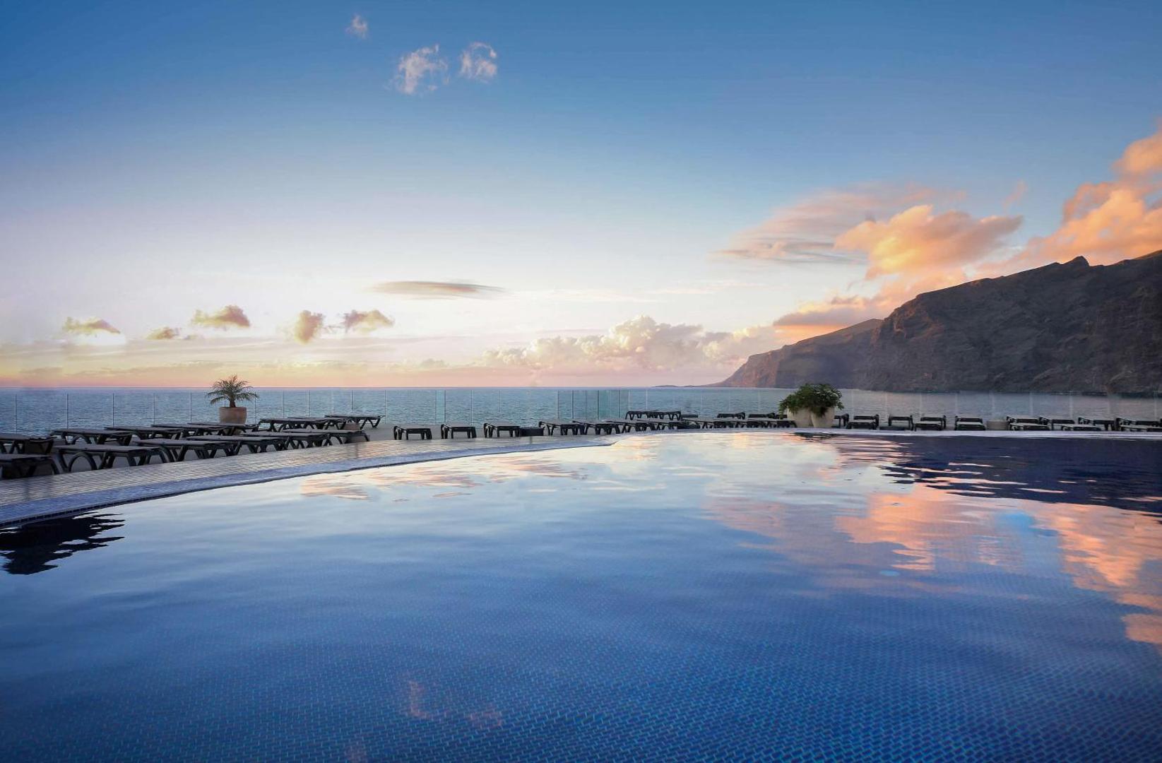 Barcelo Santiago bezgalības baseins ar skatu uz Los Gigantes klintīm un okeānu saulrieta krāsās Tenerifes piekrastē