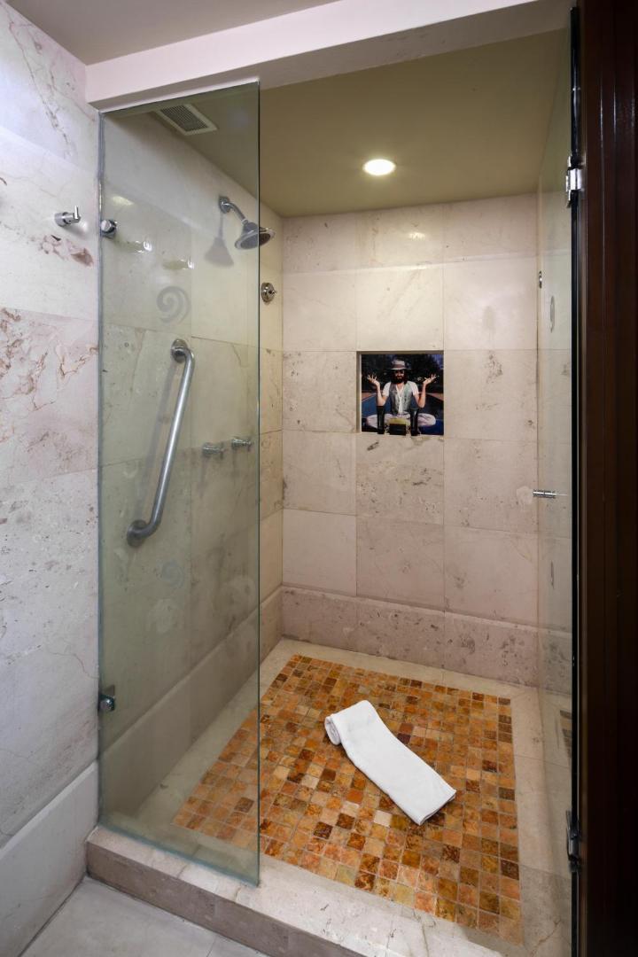 Hard Rock Hotel Cancun dušas telpa ar stikla sienu, akmens mozaīkas grīdu un unikālu mākslas darbu sienas nišā