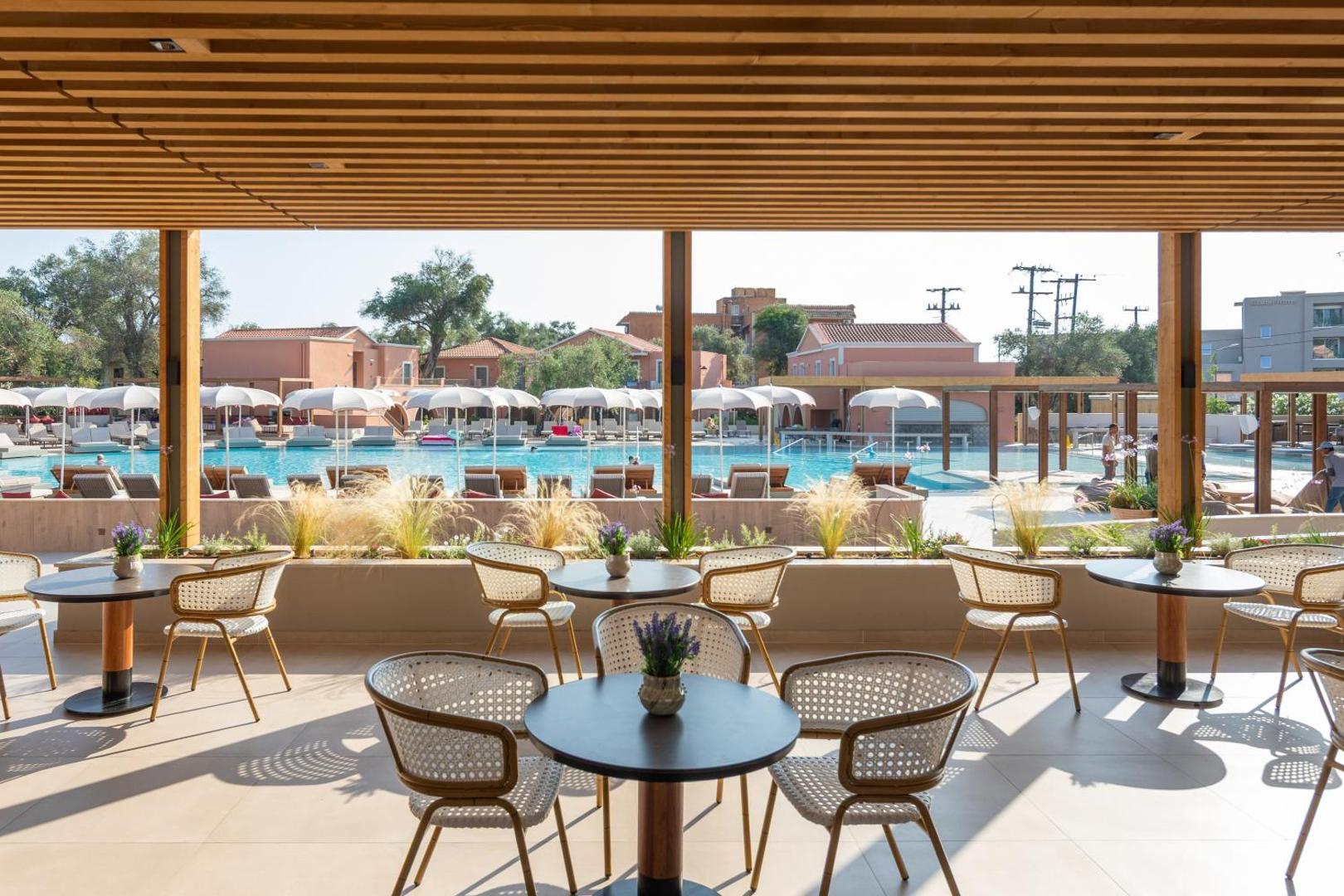 Sentido Apollo Palace āra terase ar moderniem pītiem krēsliem un skatu uz plašu baseinu, saulessargiem un viesnīcas korpusiem