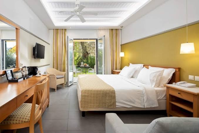 Sentido Apollo Palace viesnīcas numurs ar klasisku koka apdari, divguļamo gultu un izeju uz dārza terasi Korfu salā