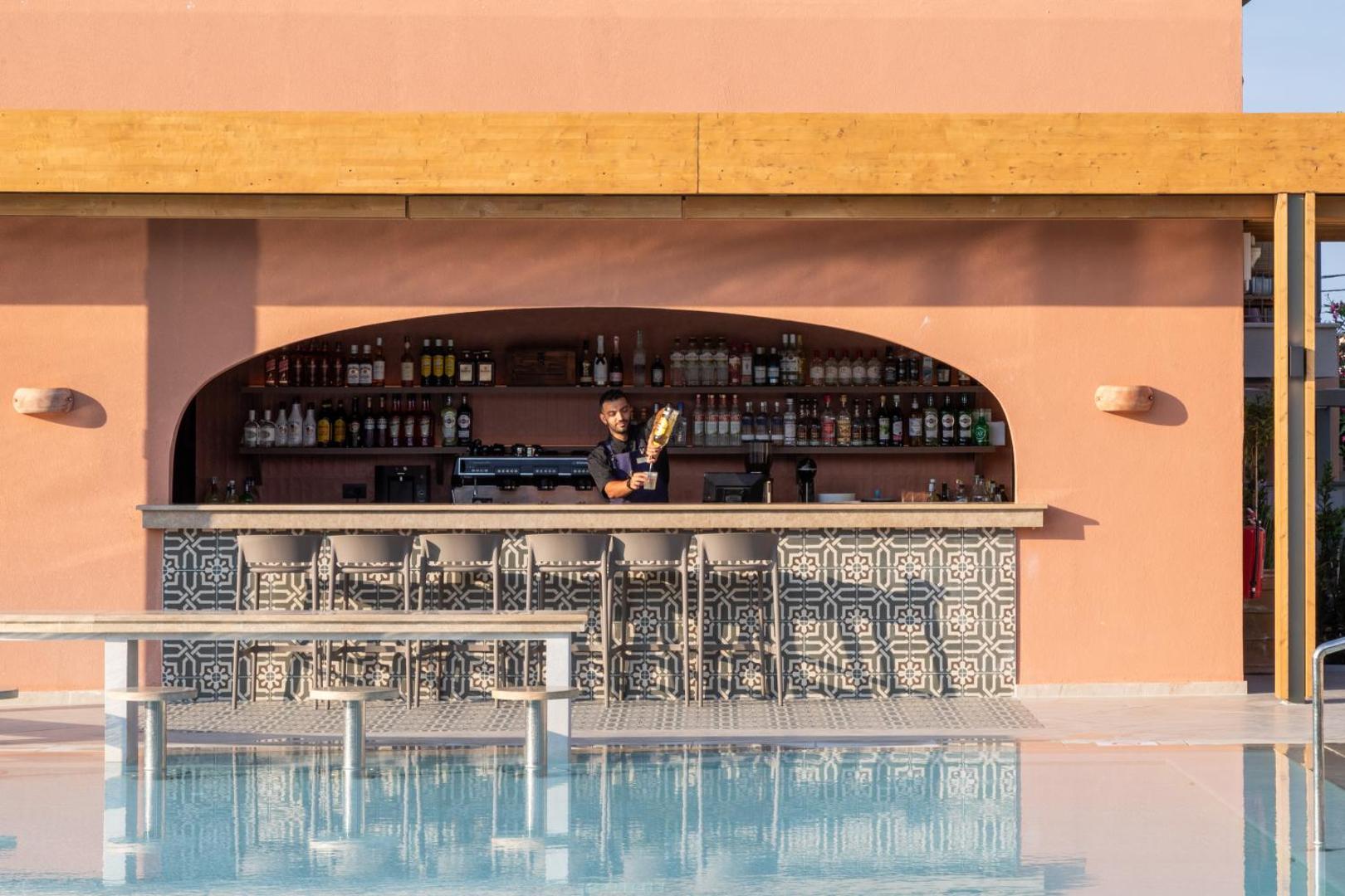 Sentido Apollo Palace bārs pie baseina ar rakstainu flīžu apdari un bārmeni darbībā — atspirdzinājumi pie ūdens Korfu kūrortā