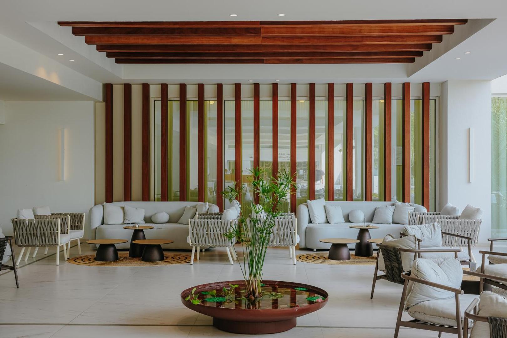 Nissiblu Beach Resort plašā lobby atpūtas zona ar dizaina dīvāniem, koka elementiem un dekoratīvu ūdens baseinu centrā