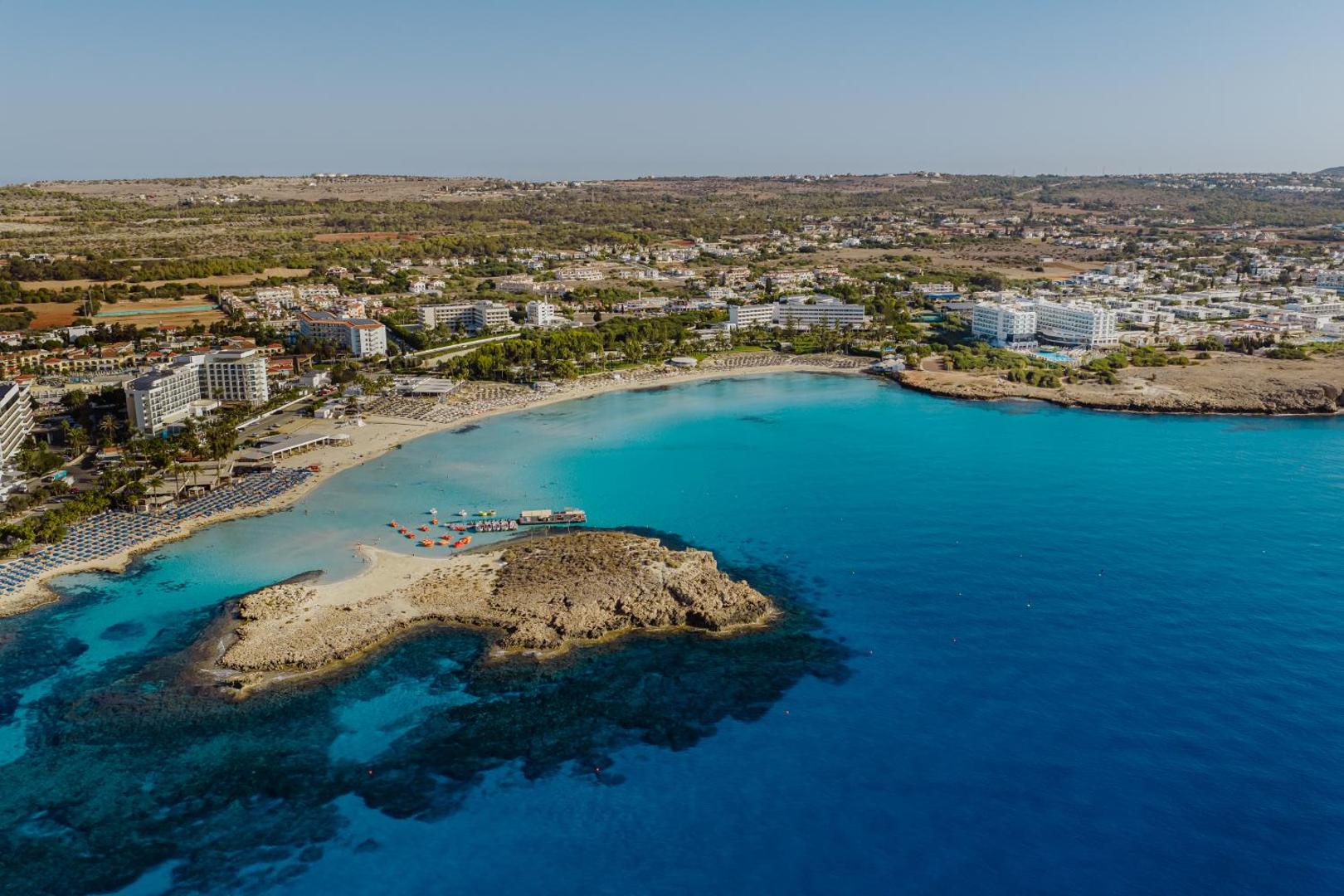 Nissiblu Beach Resort skats no putna lidojuma uz Nissi pludmali Aijanapā, Kiprā — tirkīzzils ūdens, smilšu josla un kūrorta apkaime