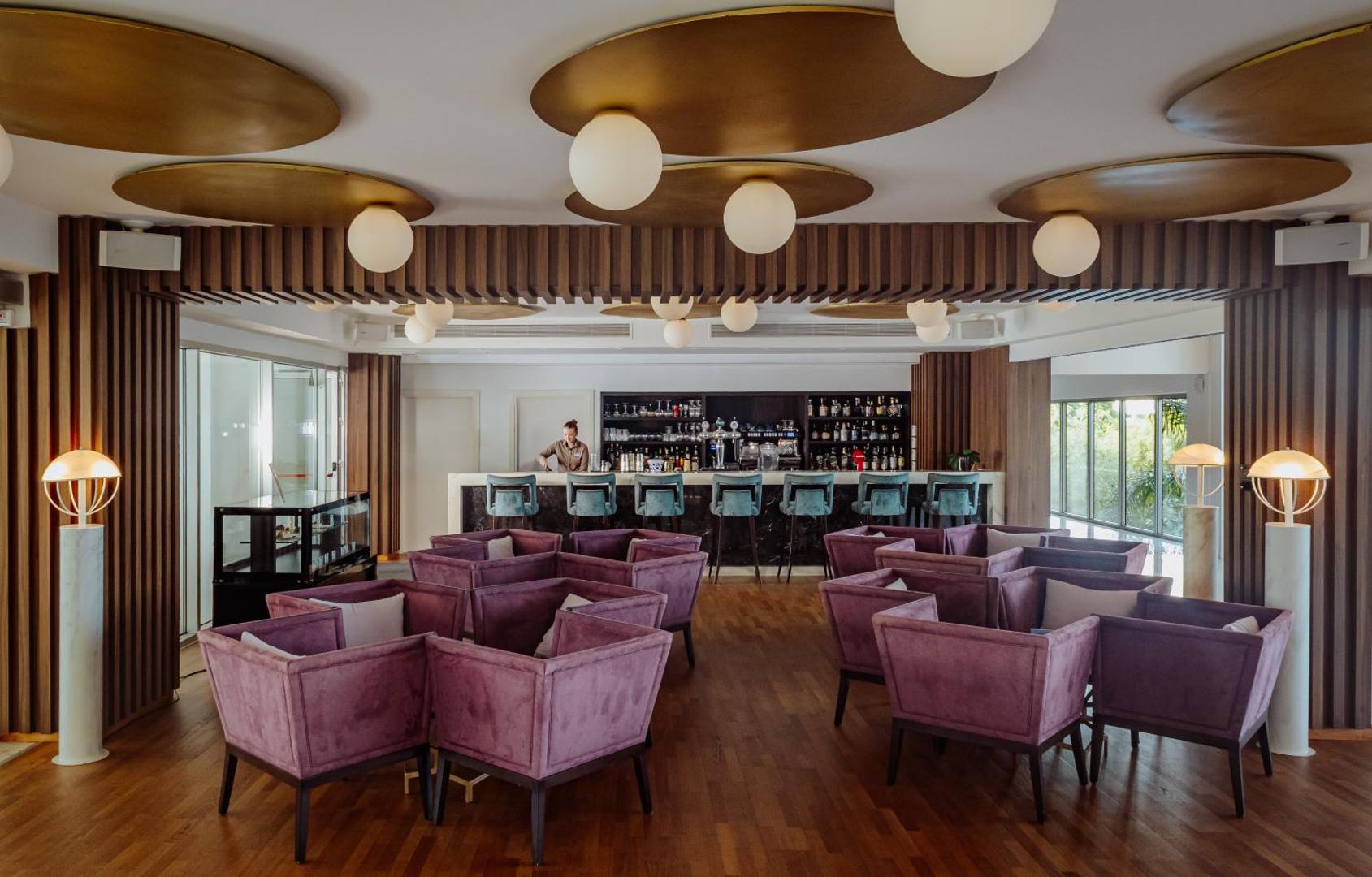 Nissiblu Beach Resort stilīgais bārs ar violetiem samta atpūtas krēsliem, koka grīdu un moderniem griestu dekoriem
