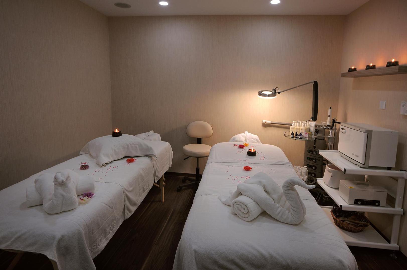 Nestor Hotel spa centra masāžas telpa ar divām kušetēm, svecēm un dekoratīviem dvieļiem mierīgai atpūtai Aijanapā, Kiprā