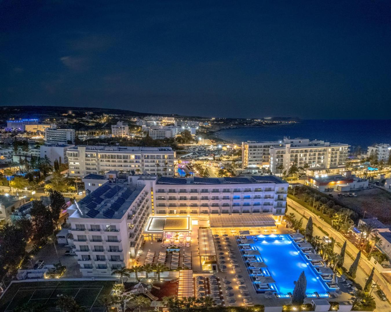 Nestor Hotel nakts skats no augšas — izgaismots āra baseins, atpūtas zona un pilsētas gaismas Aijanapas piekrastē