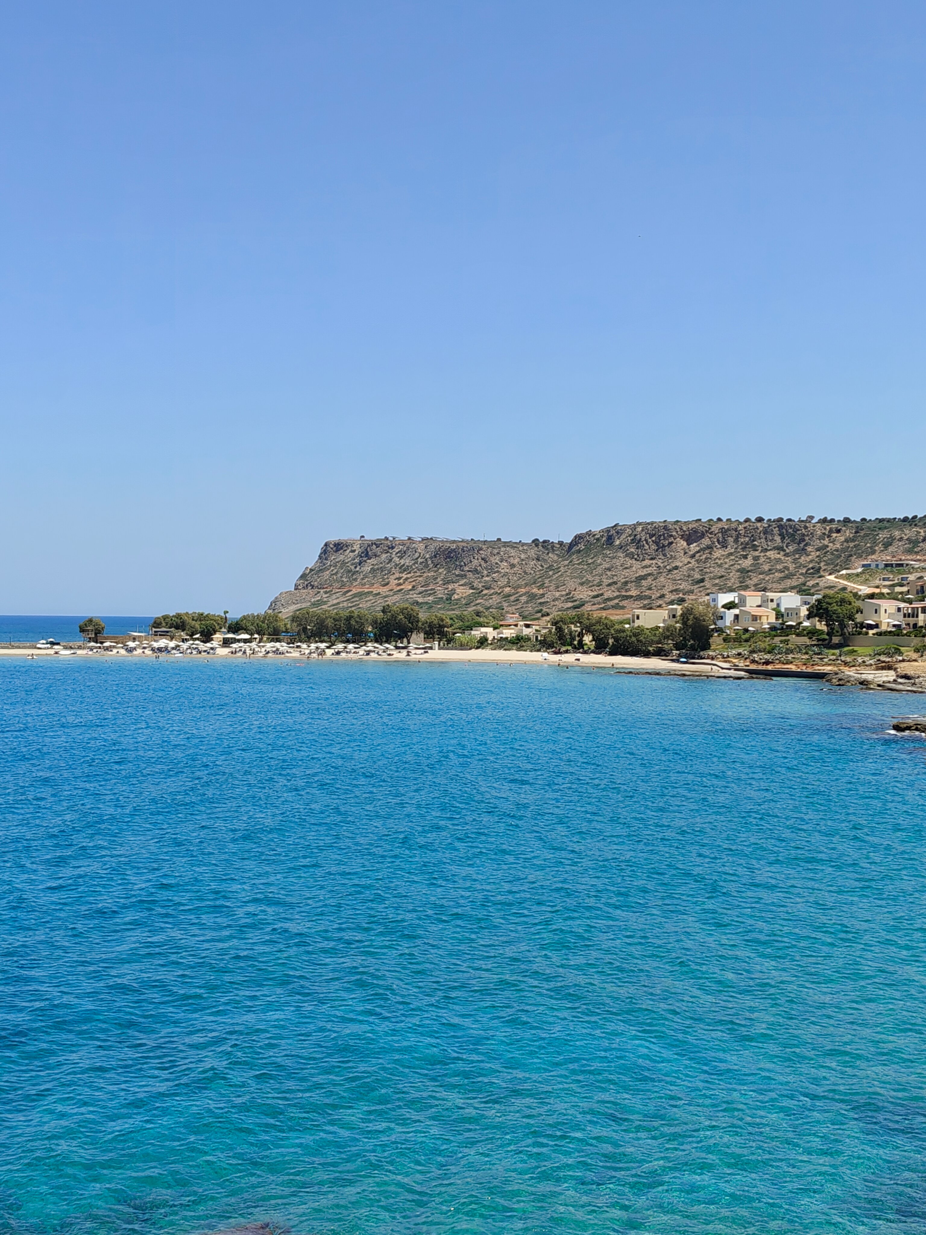 Skats uz Enorme Santanna Island piekrasti un pludmali ar gaišām smiltīm, klintīm un dzidru, zilu jūras ūdeni.