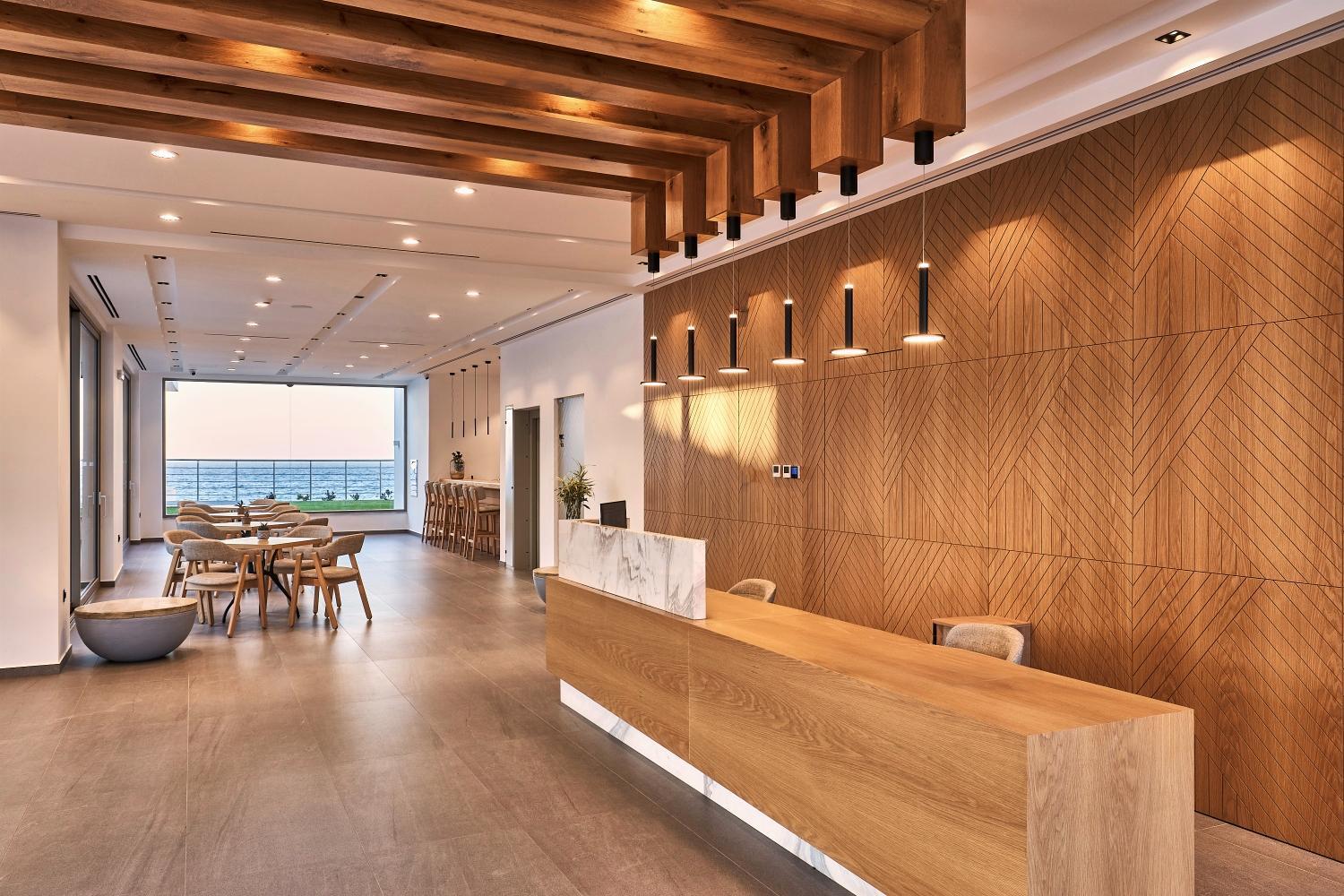 Enorme Santanna Island viesnīcas lobby un recepcijas zona ar koka apdari, modernām lampām un skatu uz jūru fonā.