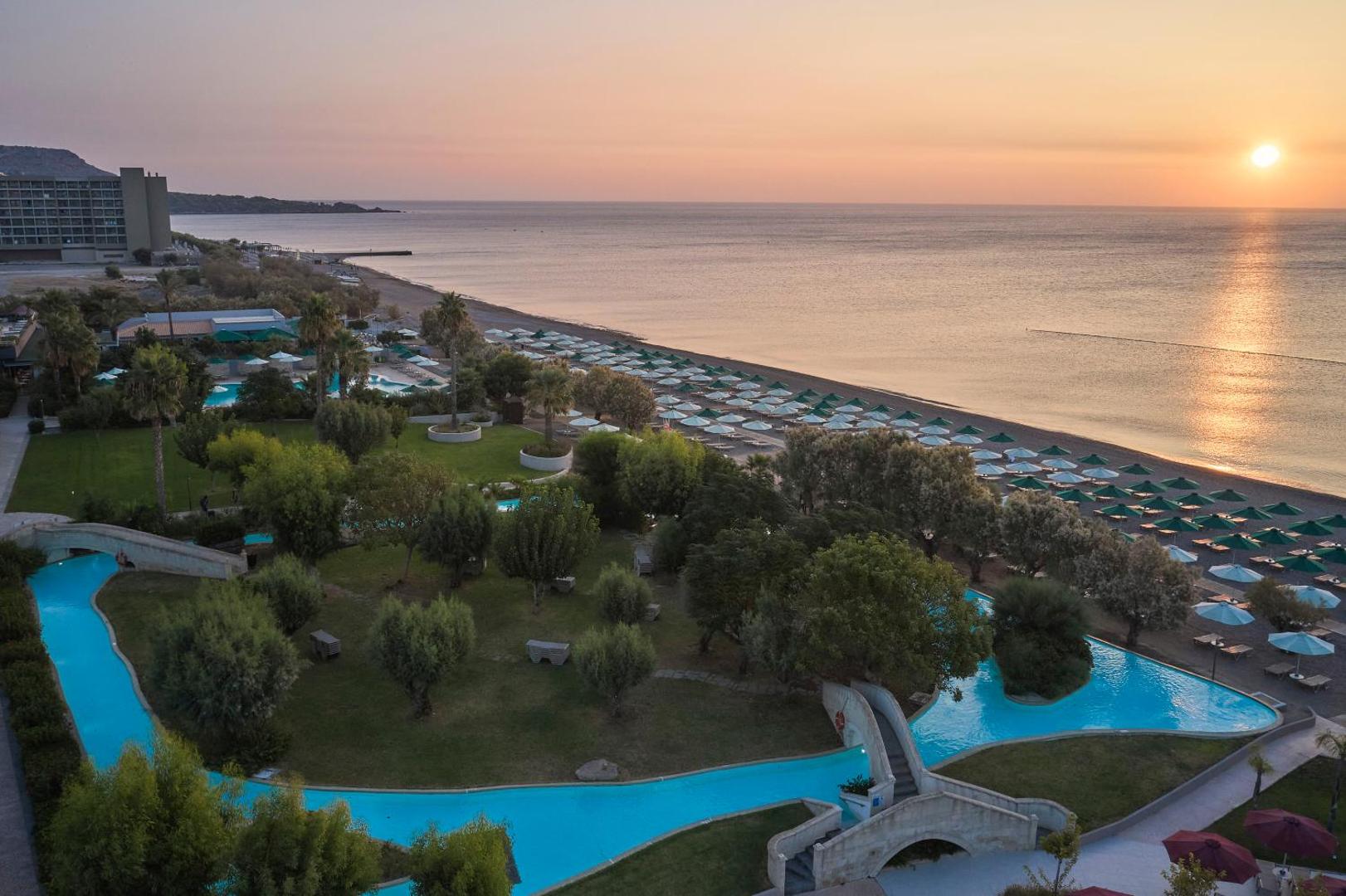 Skats no augšas uz Esperos Mare Resort & Spa dārzu, baseiniem un pludmali saulrietā.