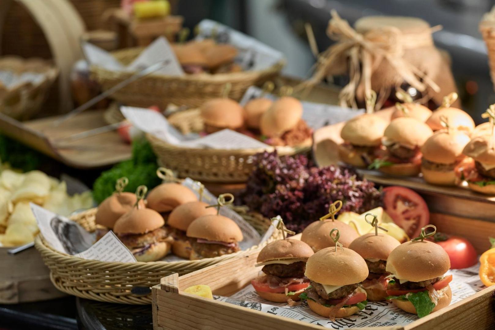 Daudzveidīgi mini burgeri servēti pītos groziņos uz bufetes galda.