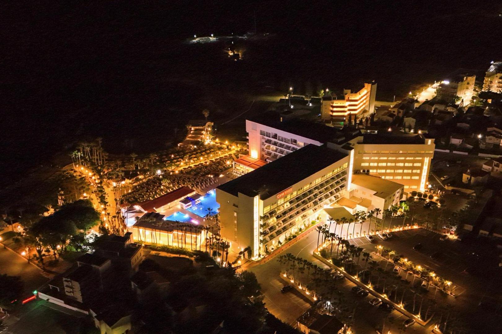 Cavo Maris Beach Hotel nakts skats no augšas — izgaismota viesnīcas ēka, baseini un Protarasas pilsētas gaismas