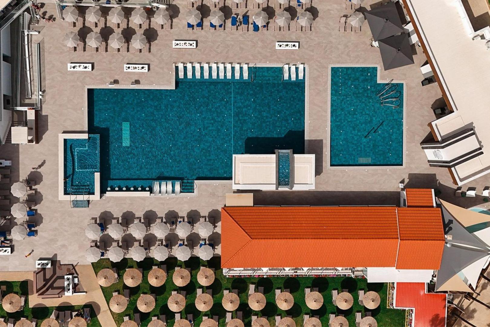 Cavo Maris Beach viesnīcas galvenais baseins no putna lidojuma Protarasā, Kiprā — skats uz sauļošanās zonu ar saulessargiem un atpūtas krēsliem