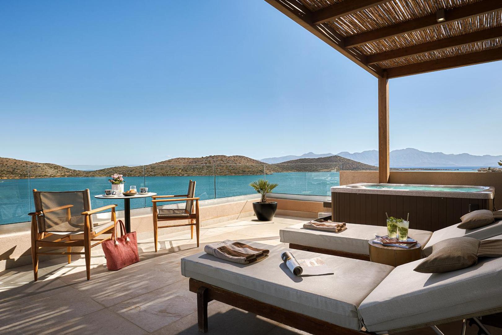 Enorme Infinity Elounda viesnīcas terase ar džakuzi, sauļošanās krēsliem un panorāmas skatu uz Mirabello līci Elundā, Krētā.