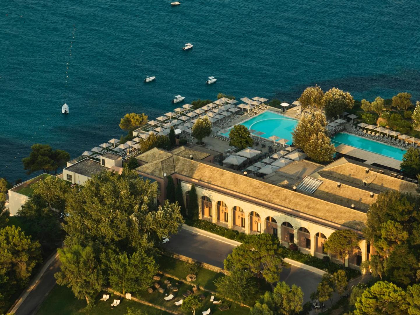 Atlantica Grand Mediterraneo Resort galvenā ēka ar arkām un āra baseiniem pie pašas jūras, ko ieskauj zaļi koki un atpūtas zona.