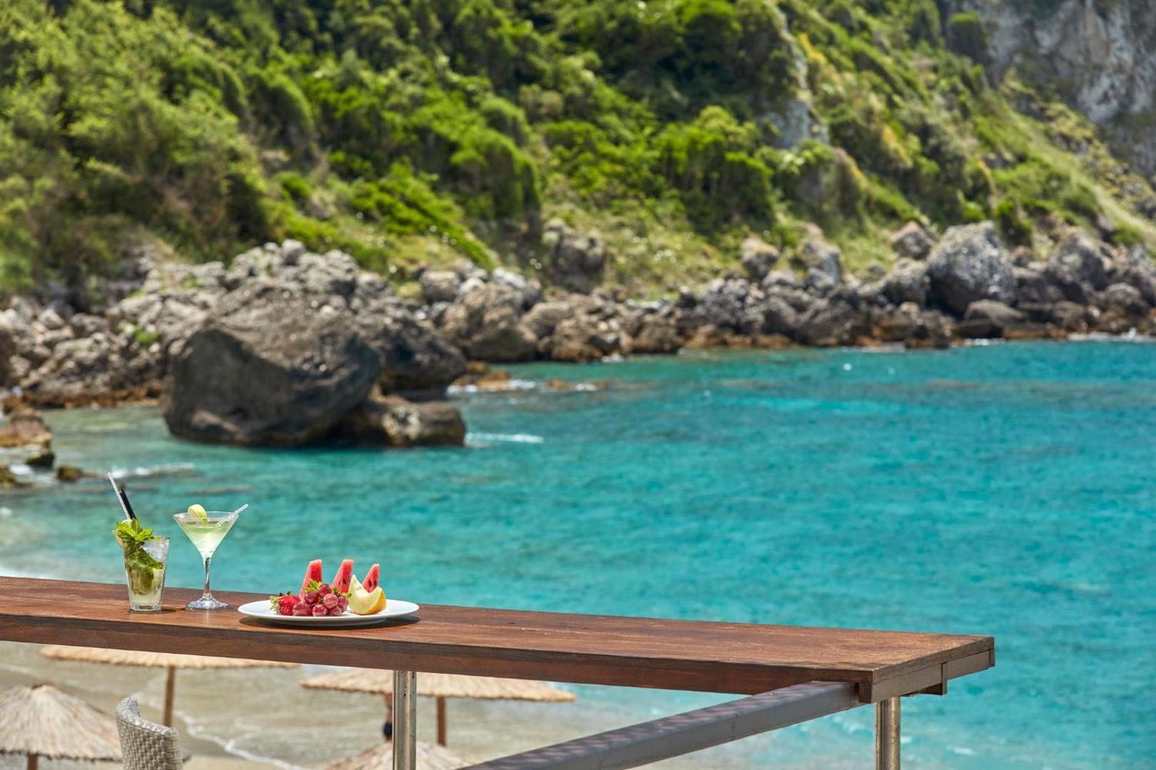 Kokteiļi un augļu plate uz Atlantica Grand Mediterraneo Resort bāra letes ar skatu uz tirkīzzilo jūru un klintīm