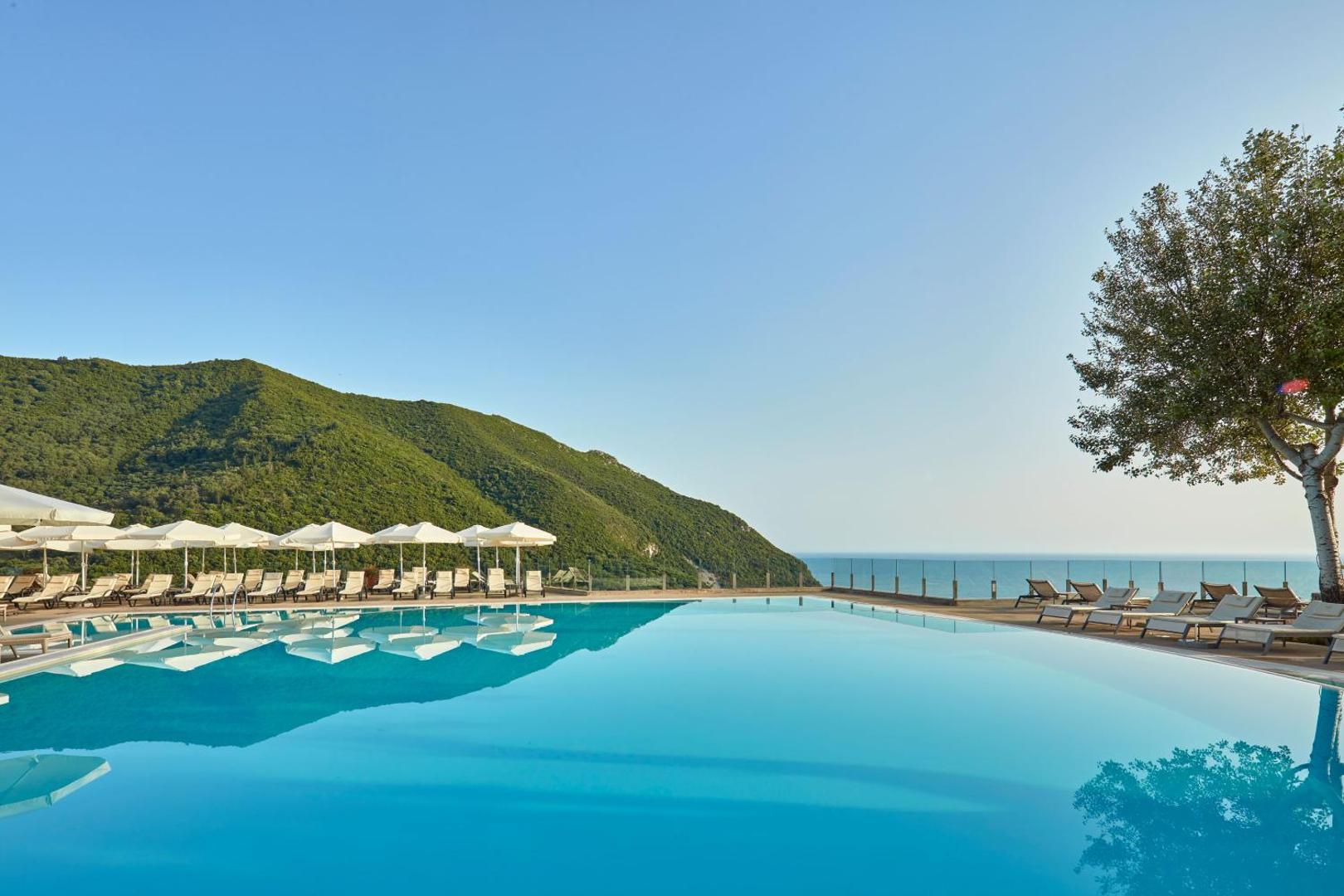 Atlantica Grand Mediterraneo Resort bezgalības baseins ar skatu uz Jonijas jūru un zaļajiem kalniem Korfu piekrastē, Grieķijā.