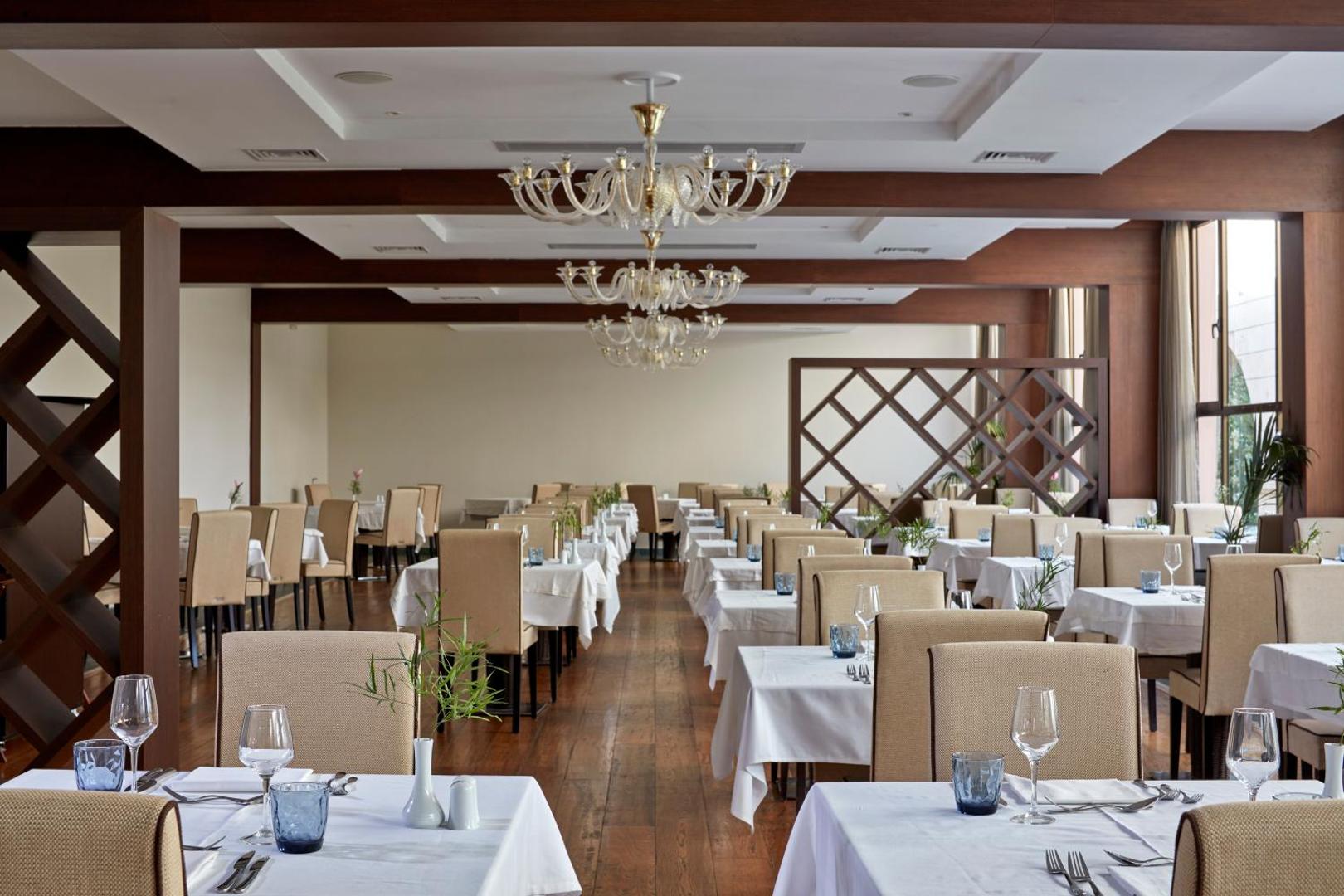 Atlantica Grand Mediterraneo Resort galvenais restorāns ar eleganti klātiem galdiem, koka grīdu un greznām lustrām Korfu salā