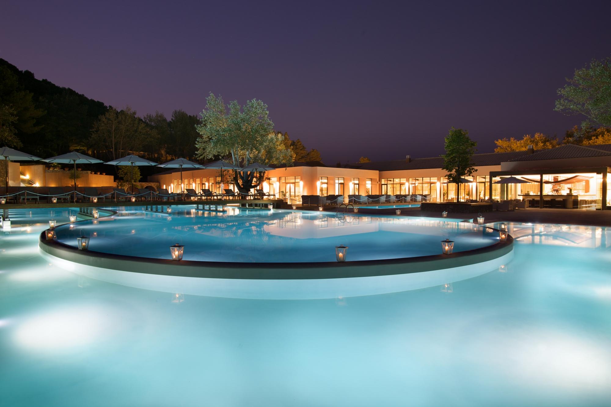 Atlantica Grand Mediterraneo Resort izgaismots āra baseins vakarā ar laternām un viesnīcas ēkas gaismām tumši zilu debesu fonā.