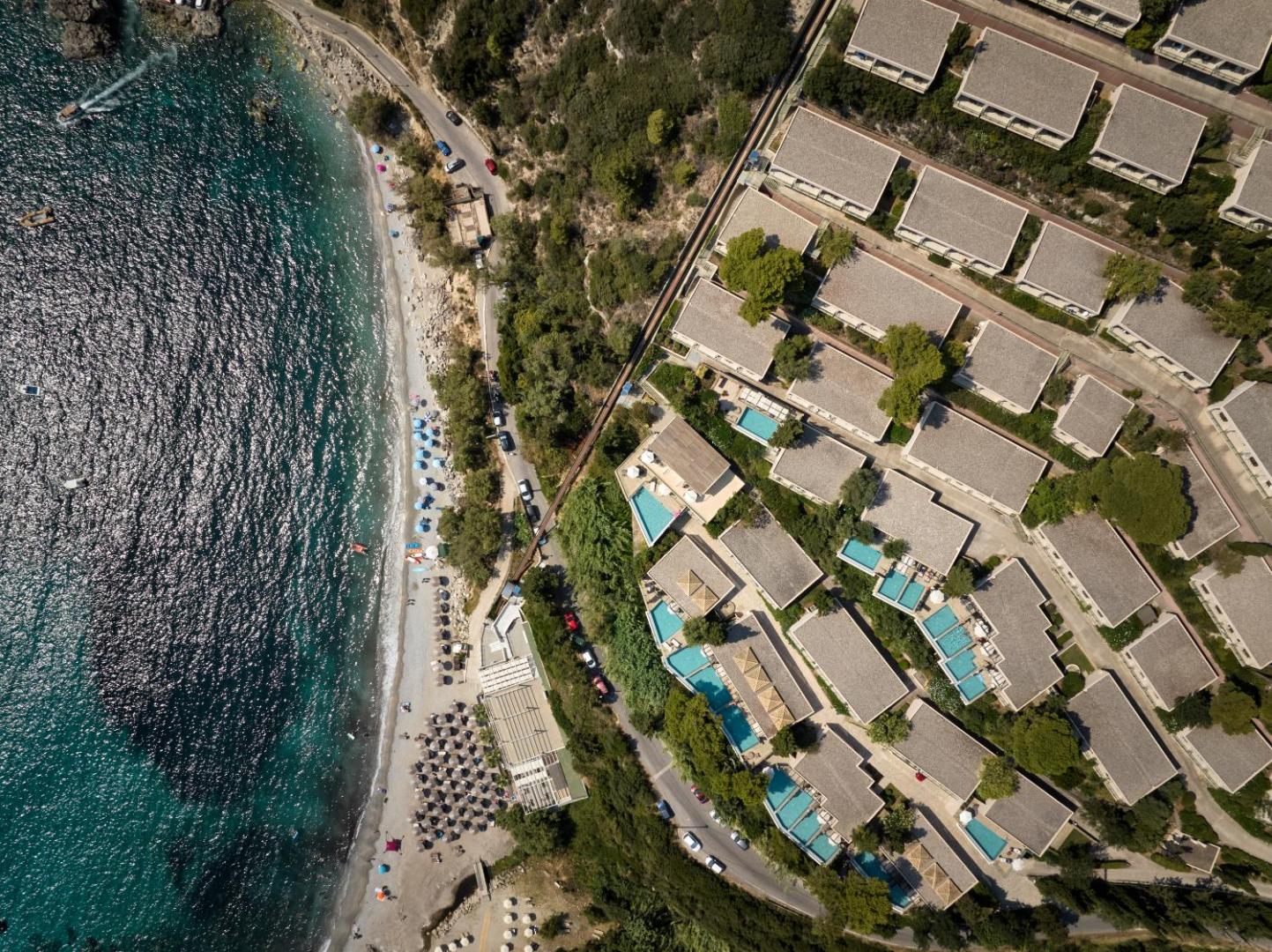Aerofoto skats uz Atlantica Grand Mediterraneo Resort privāto pludmali, saulessargiem un bungalo ar privātiem baseiniem Korfu piekrastē.