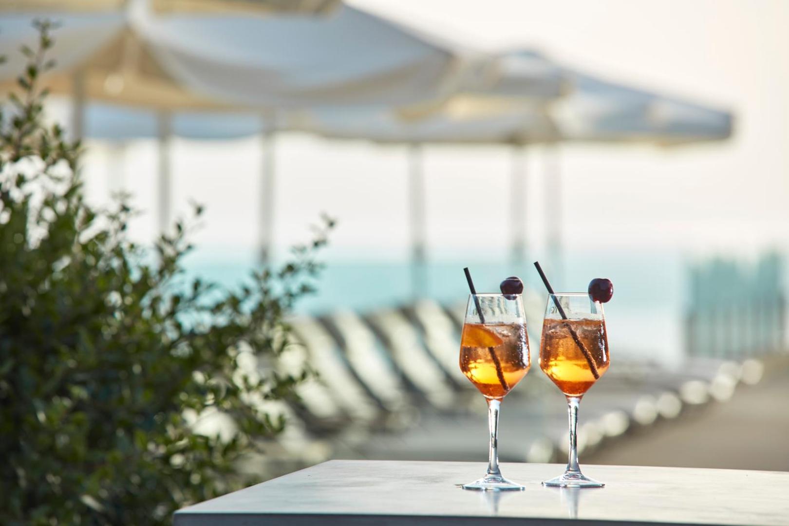 Divi atspirdzinoši kokteiļi uz galda Atlantica Grand Mediterraneo Resort pludmales bārā ar saulessargiem fonā