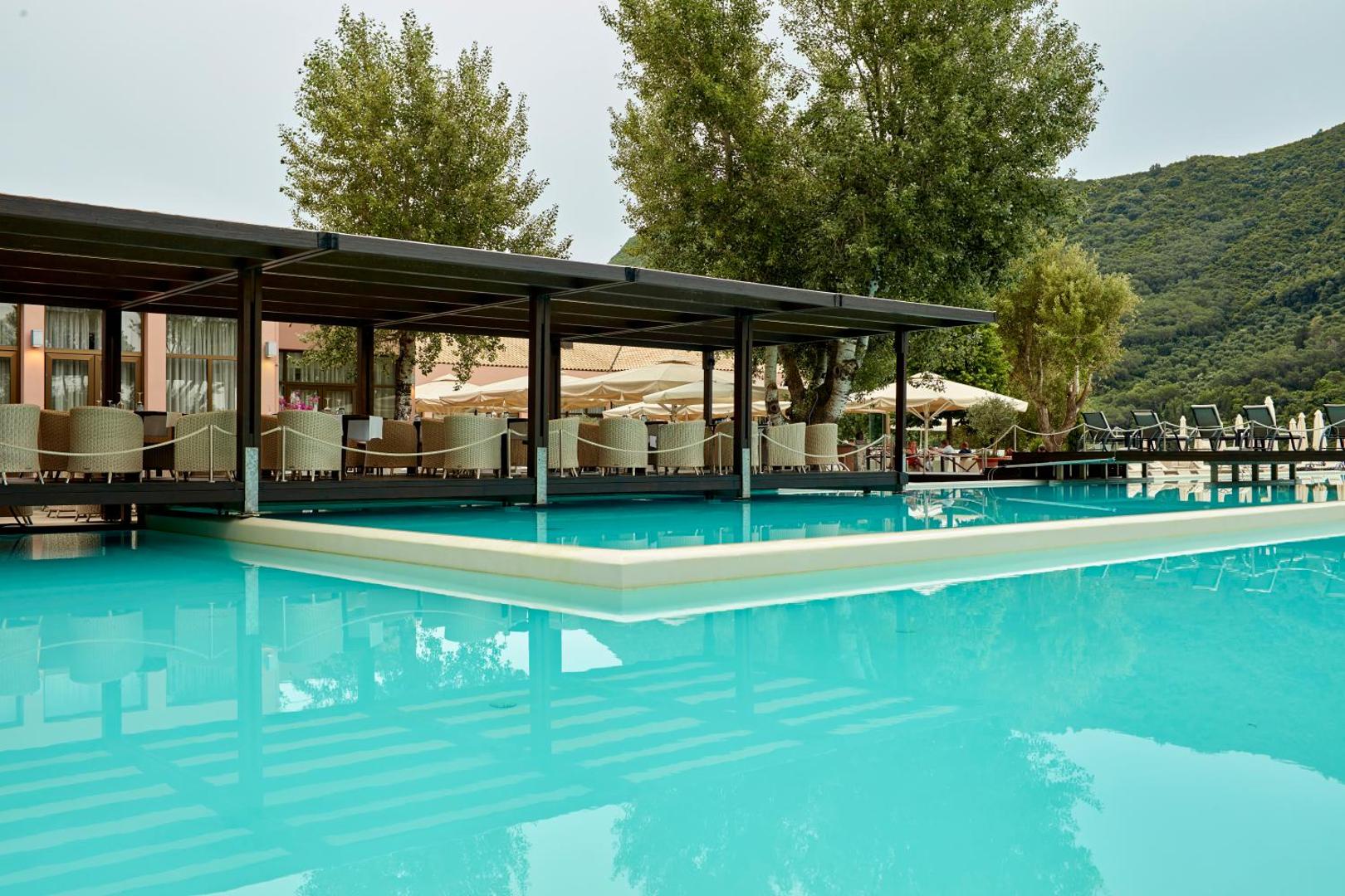 Atlantica Grand Mediterraneo Resort restorāna terase virs baseina ūdens ar pītiem krēsliem un koku ieskautu apkārtni.
