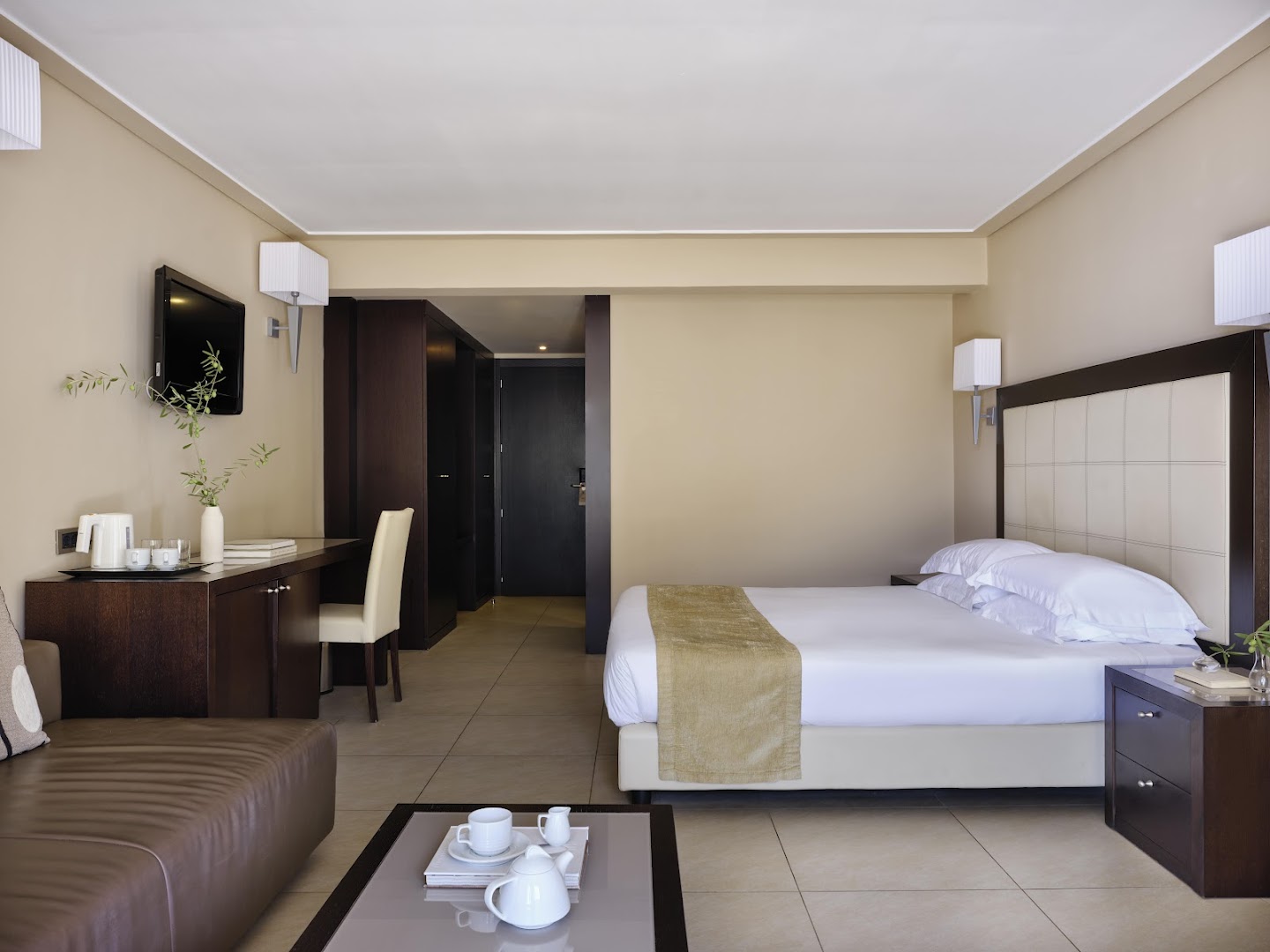 Atlantica Grand Mediterraneo Resort numura interjers ar darba zonu, dīvānu un ērtu gultu Korfu salā