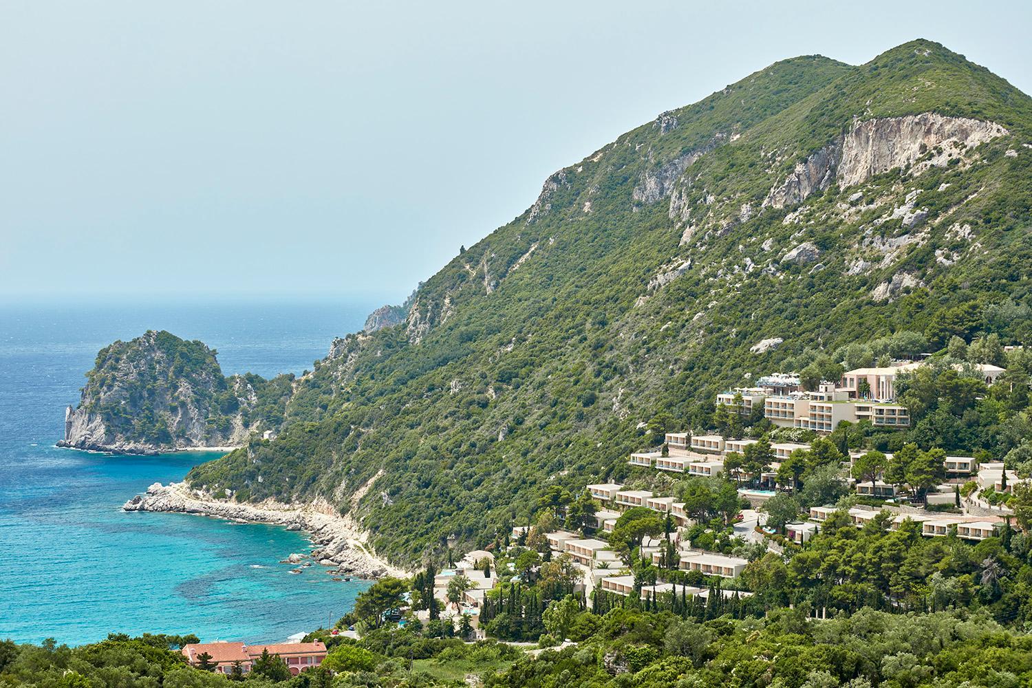 Atlantica Grand Mediterraneo Resort panorāmas skats uz viesnīcas kompleksu un Jonijas jūras piekrasti Korfu salā, Grieķijā, starp zaļiem kalniem.