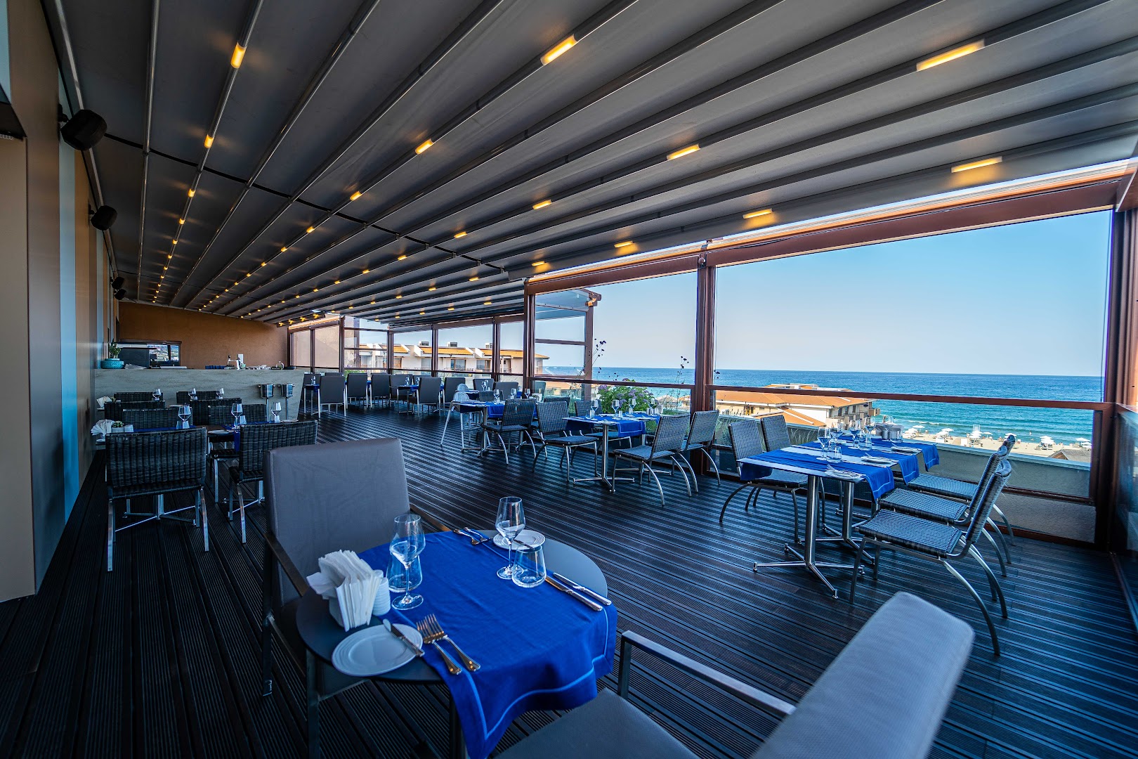 HVD Club Hotel Miramar restorāna terase ar modernām mēbelēm, ziliem galdautiem un panorāmas skatu uz jūru caur lieliem logiem.