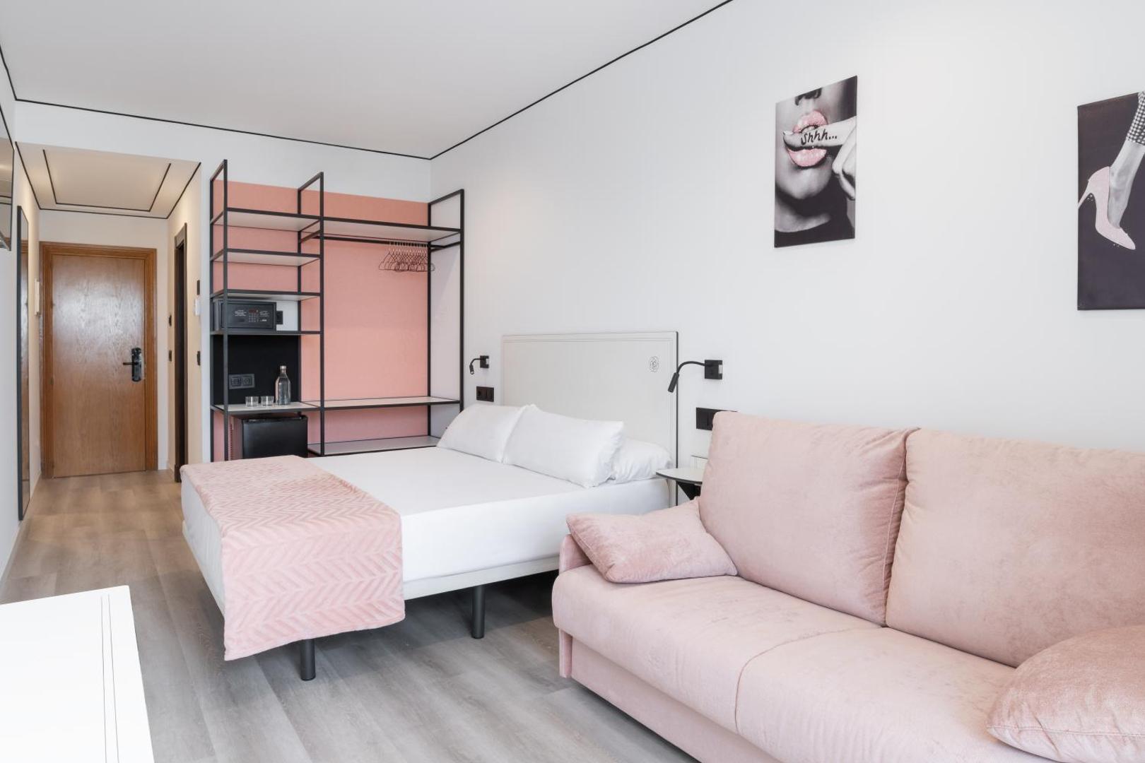 Mūsdienīgs Hotel Condesa numura interjers ar rozā dīvānu, atvērtā tipa skapi un stilīgiem sienas dekoriem Maljorkā