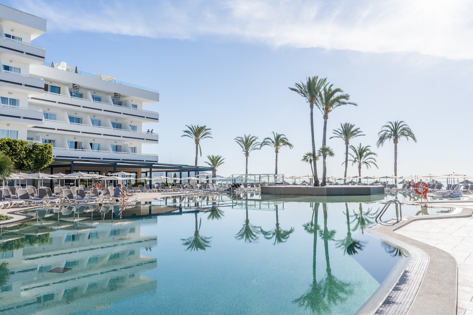 Hotel Condesa lielais āra baseins ar palmām, sauļošanās krēsliem un skatu uz jūru Maljorkas piekrastē