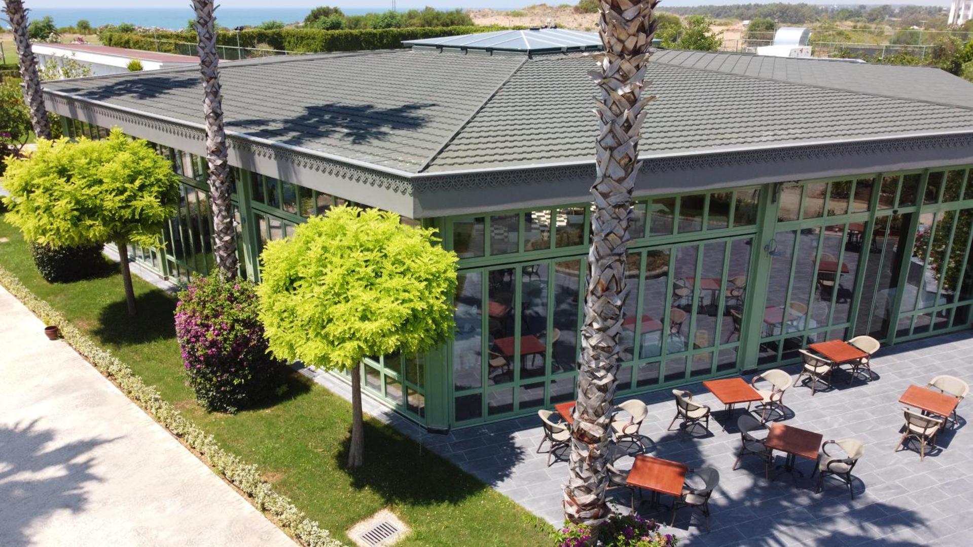 TUI Magic Life Jacaranda dārza restorāna ēka ar stiklotām sienām, āra terasi un zaļojošiem kokiem kūrorta teritorijā