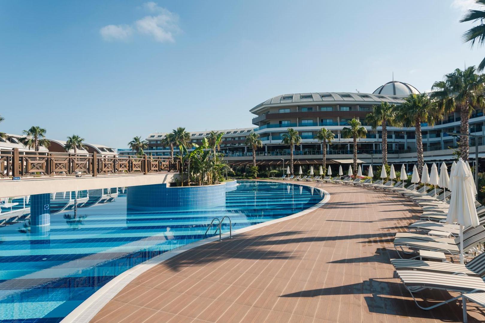 TUI Magic Life Jacaranda galvenais baseins ar zviļņiem un saulessargiem, fonā redzama modernā viesnīcas ēka un palmas